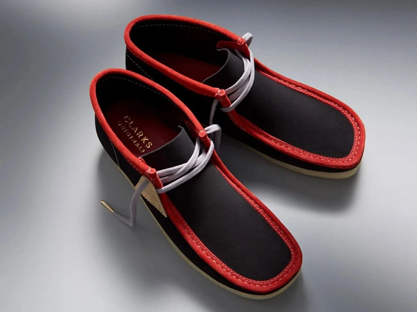 pair of black wallabee shoes with red piping seen from overhead with dramatic light