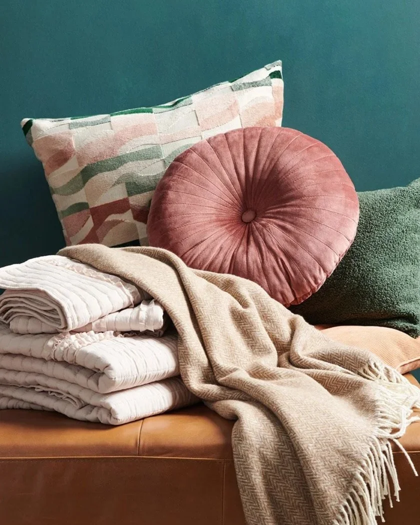pillows and blankets casually arranged against green wall on leather ottoman 