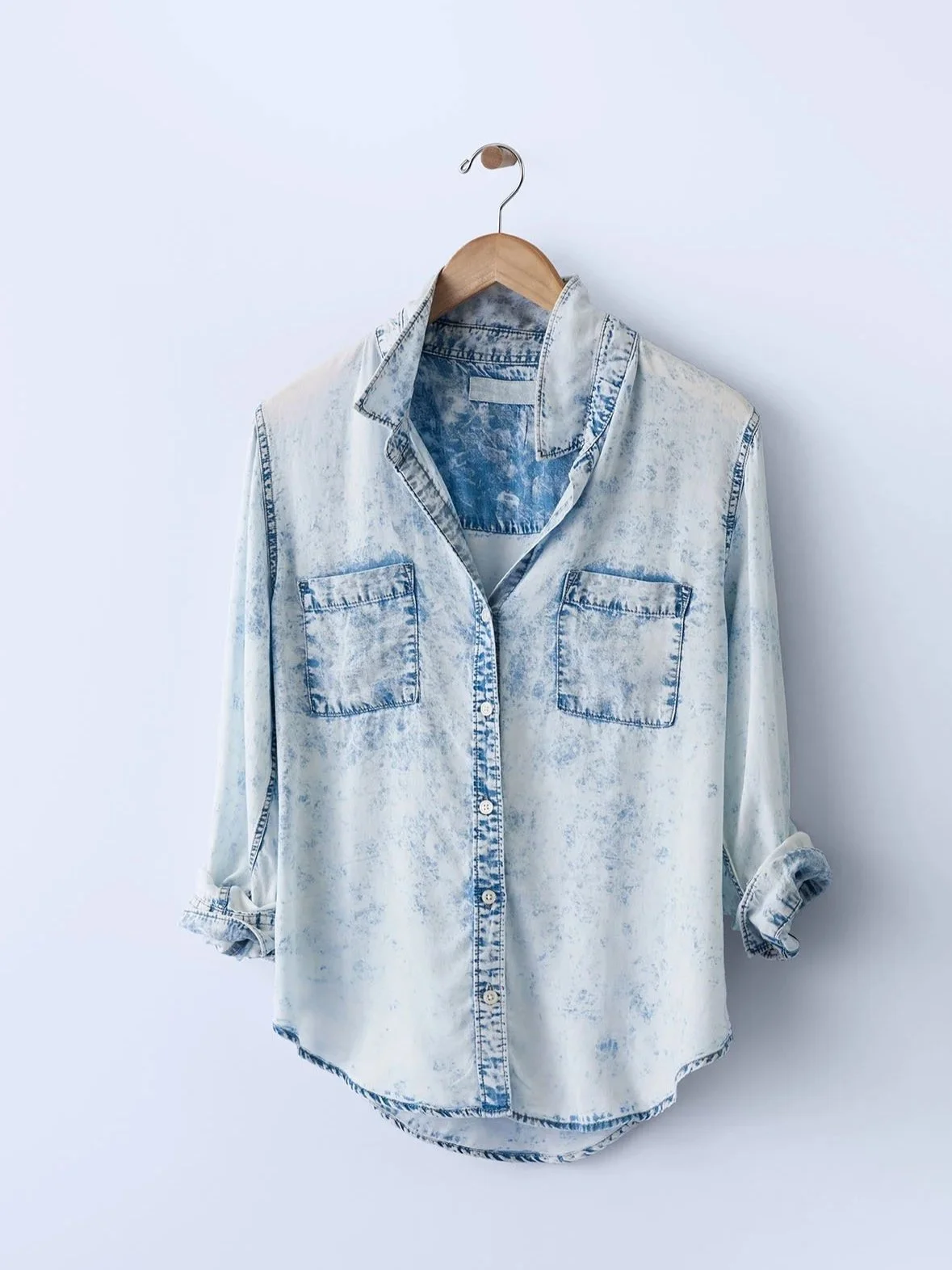 women's chambray button down shirt hung casually against blue background on modern wooden hanger 