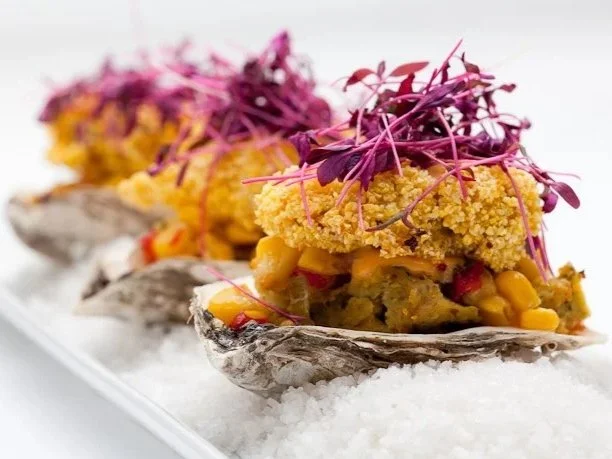 Three oysters topped with crab salad, microgreens, and edible flowers on a bed of salt.