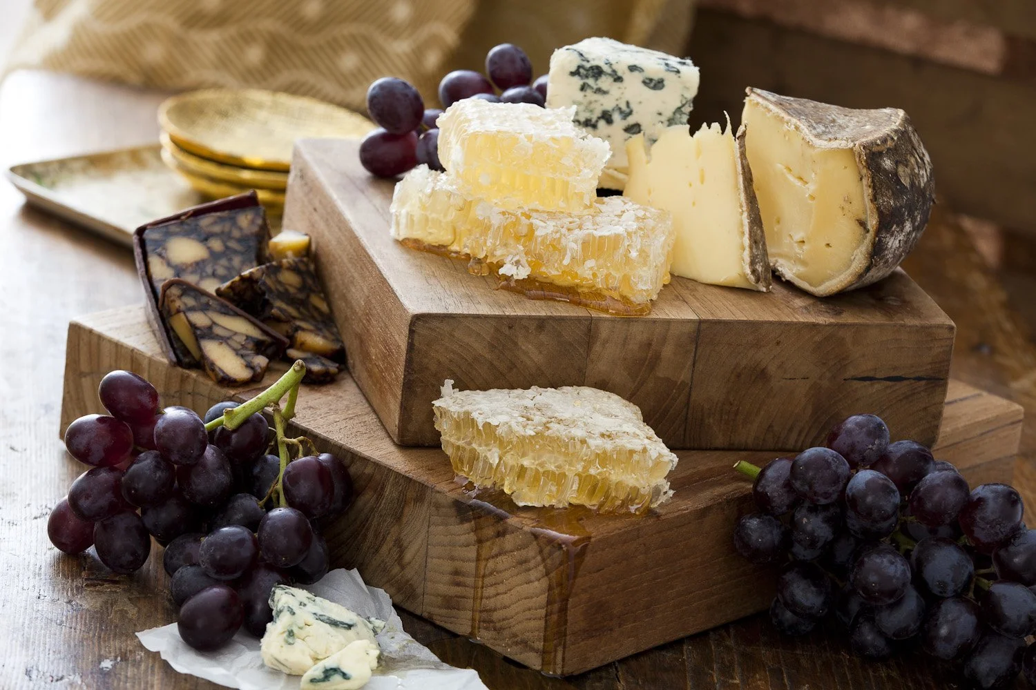 assorted cheeses with honey and grapes arranged on wood blocks trays