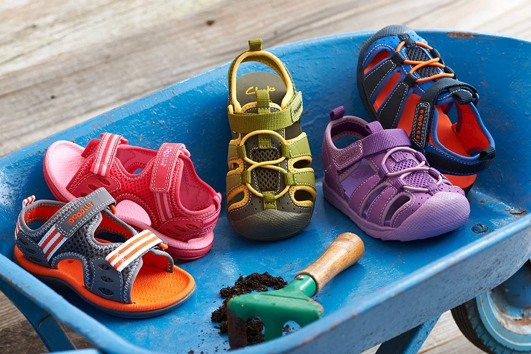 toddler colorful water shoes arranged in blue wheelbarrow with toy mini garden rake tool