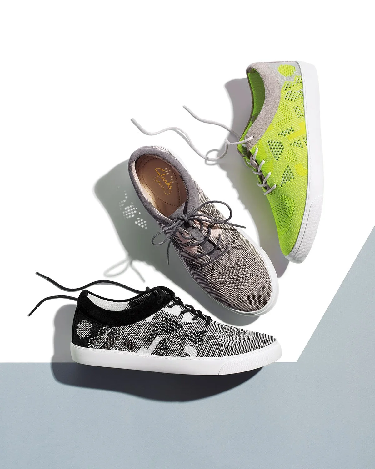 dynamic arrangement of three single casual shoes with floating laces and strong shadow light on grey and white shape background