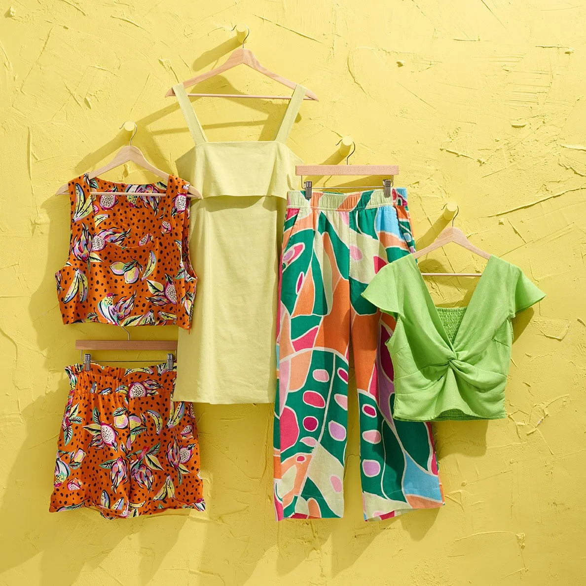 tropical inspired women's summer clothing on hangers set against yellow stucco wall 