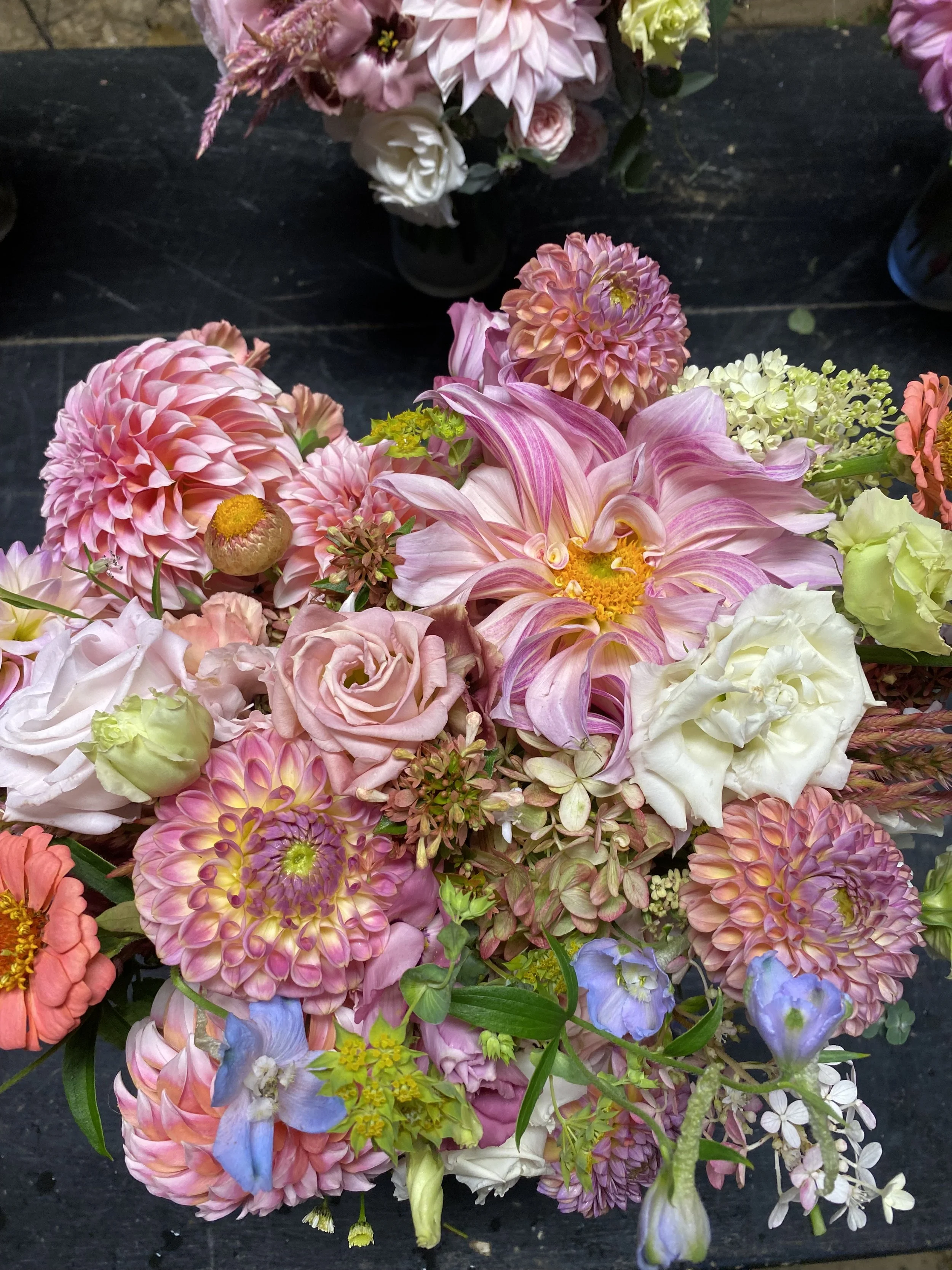 Beautiful bouquet of pink, white, and purple flowers including dahlias, roses, and lilies on a dark surface.