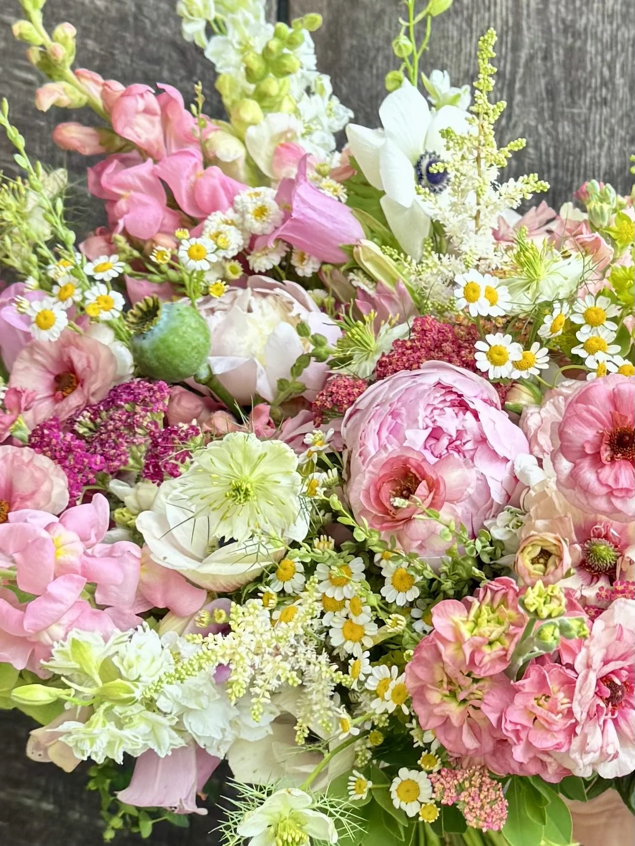 A colorful bouquet of various pink, white, and yellow flowers against a dark wooden background.