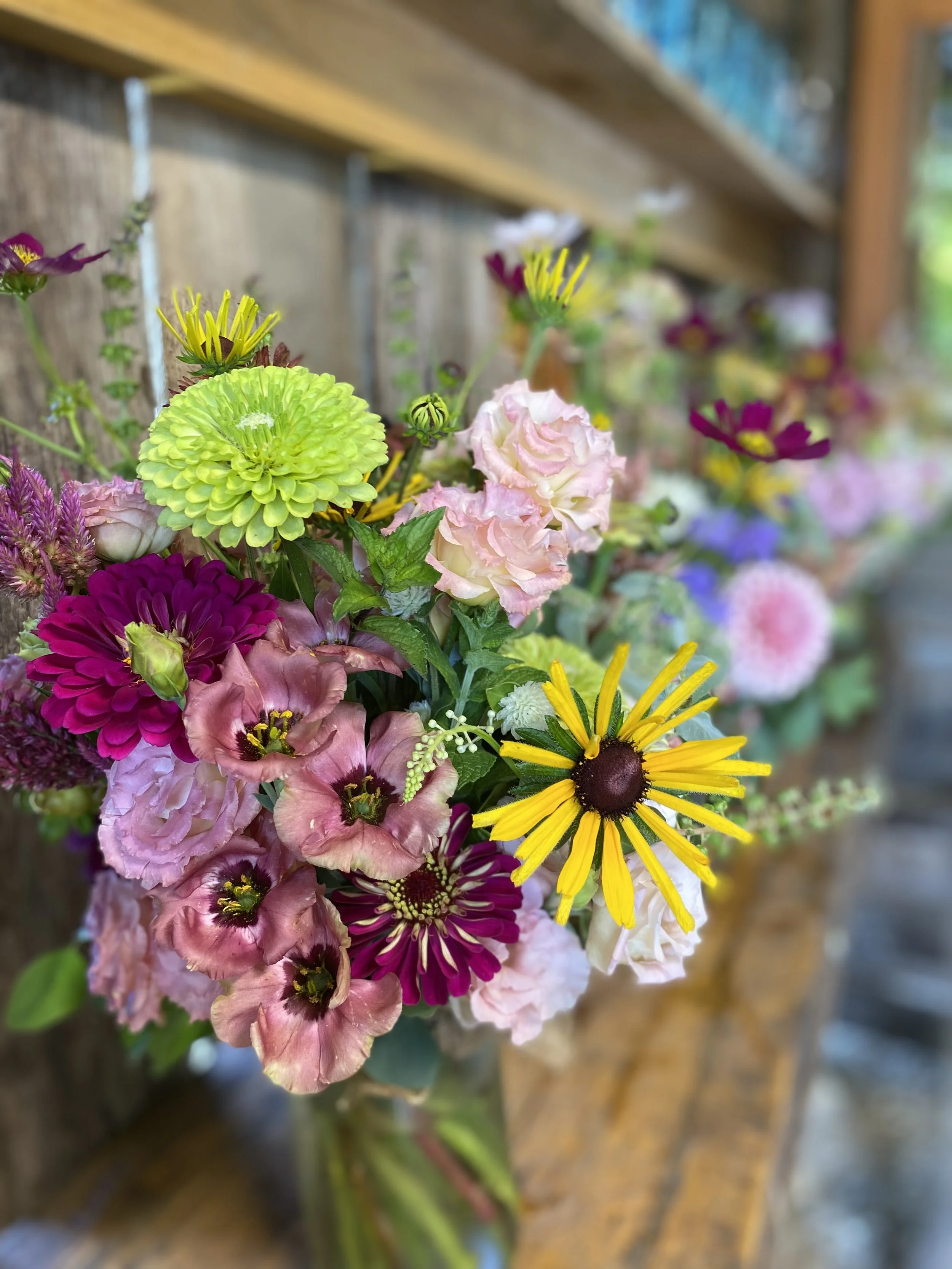 A colorful bouquet of various flowers including yellow, purple, pink, and green flowers set on a wooden surface outdoors.