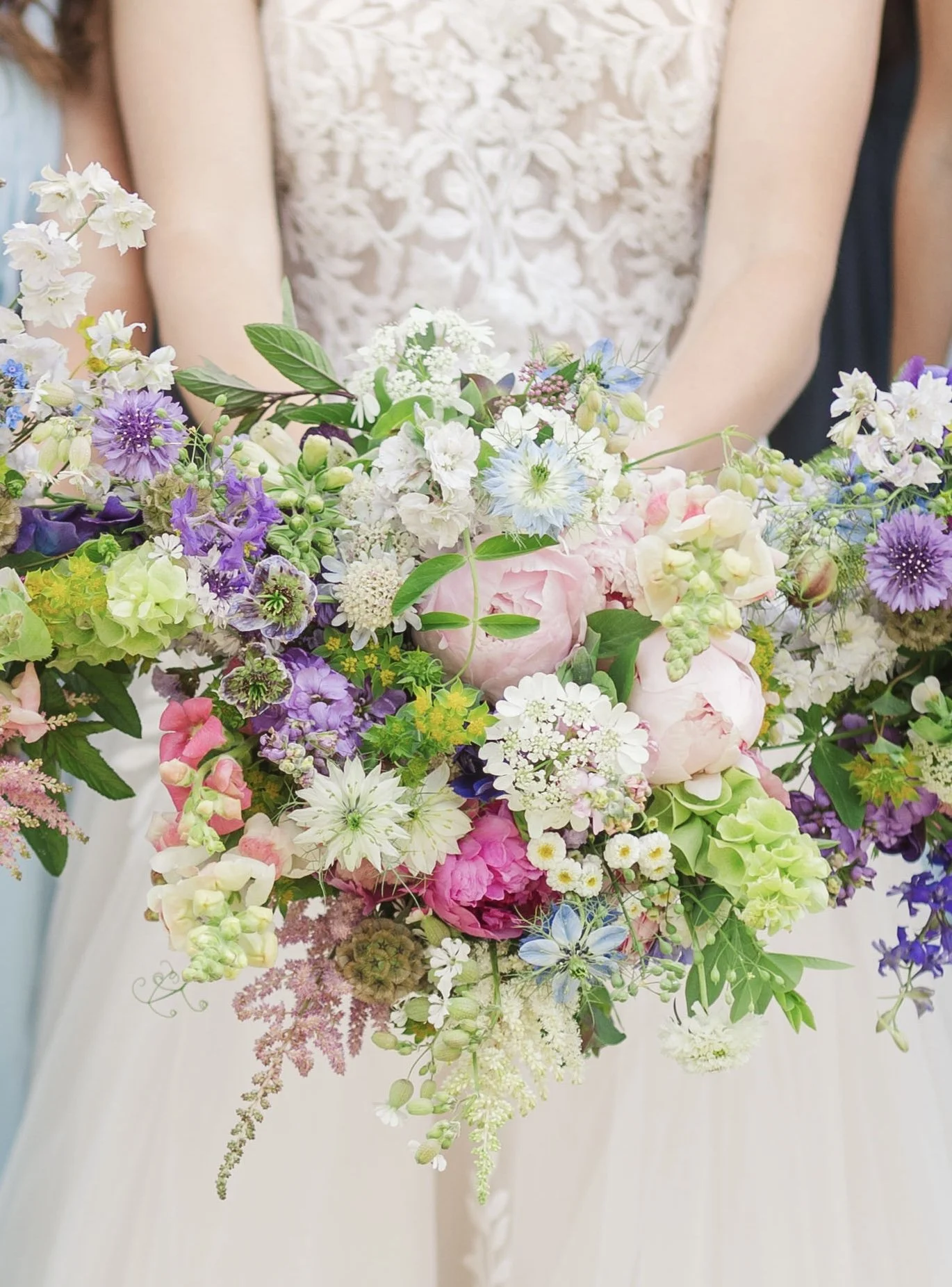 A person holding a large bouquet of mixed colorful flowers including pink, purple, white, and blue blooms.