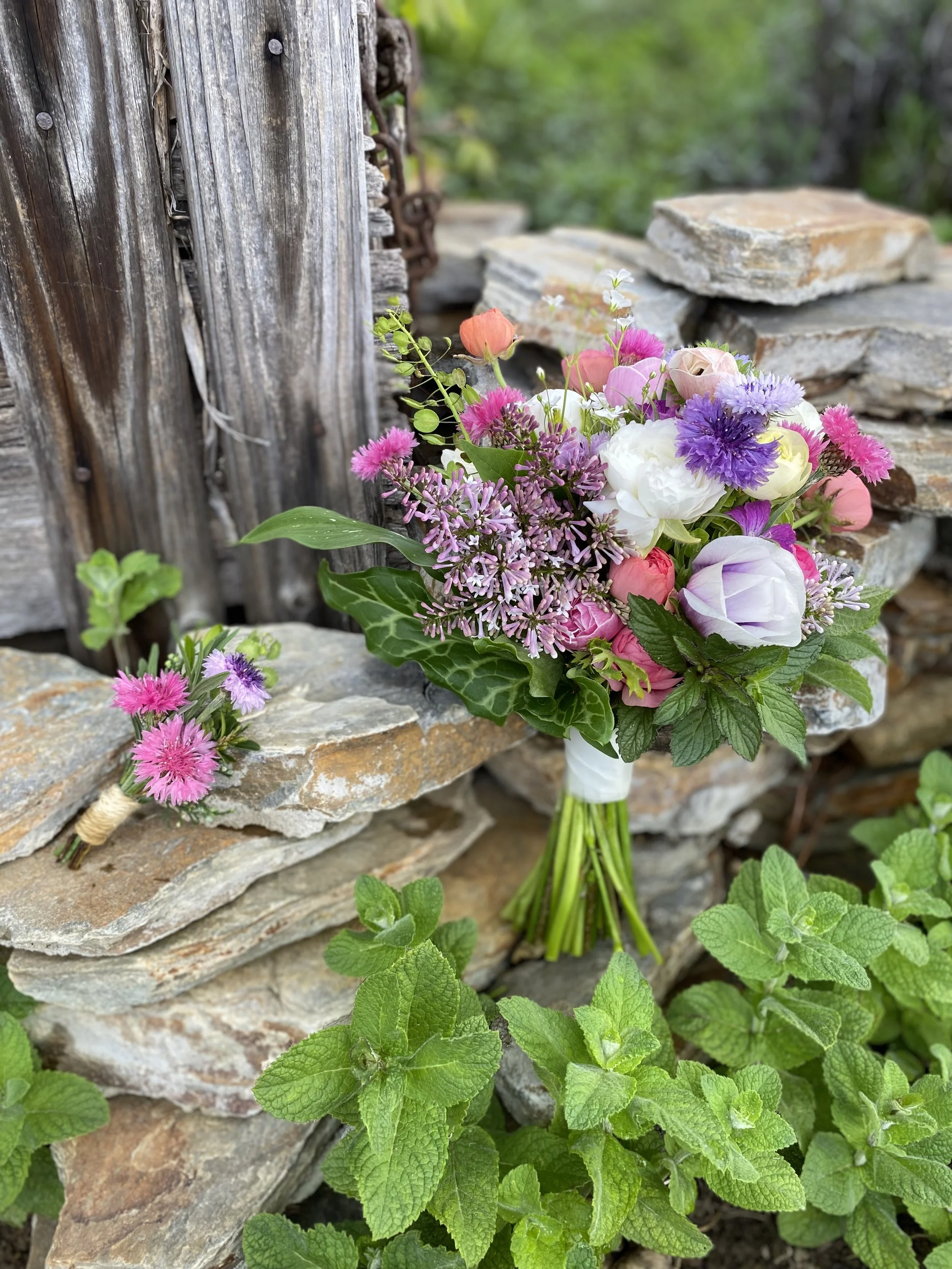 Colorful bouquet of flowers resting on a stone wall in a garden setting.