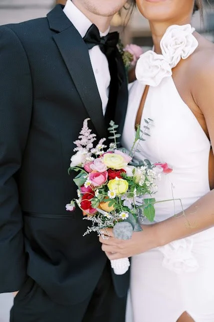 Close-up of a bride and groom at their wedding, with the bride holding a colorful bouquet of flowers and the groom dressed in a black tuxedo.