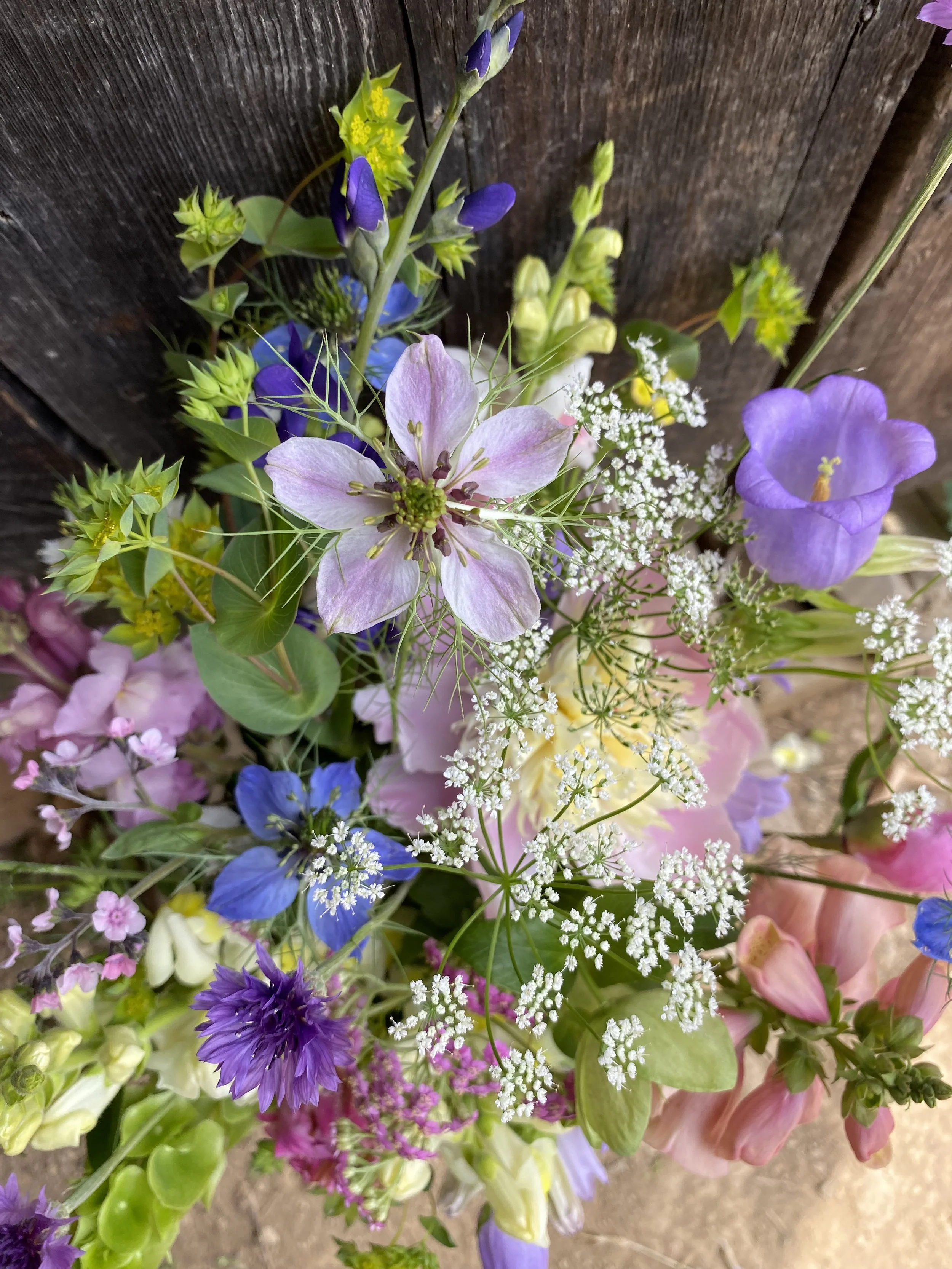 Close-up of a colorful bouquet of spring flowers including blue, purple, pink, and white blossoms against a wooden background.