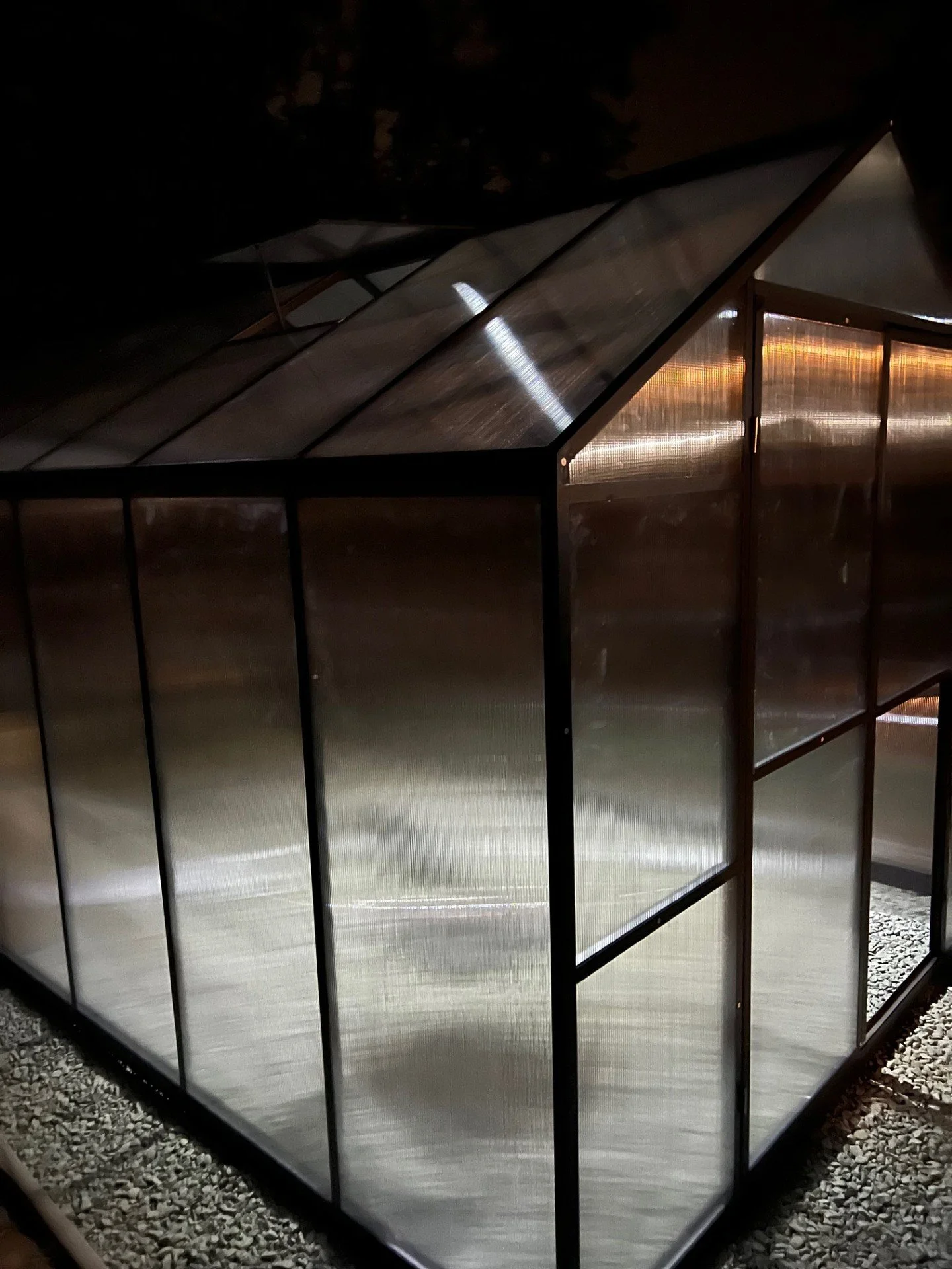 A greenhouse at night with frosted glass panels and metal framing.