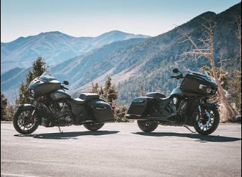 Two black touring motorcycles parked on a mountain road with a scenic mountain range in the background.