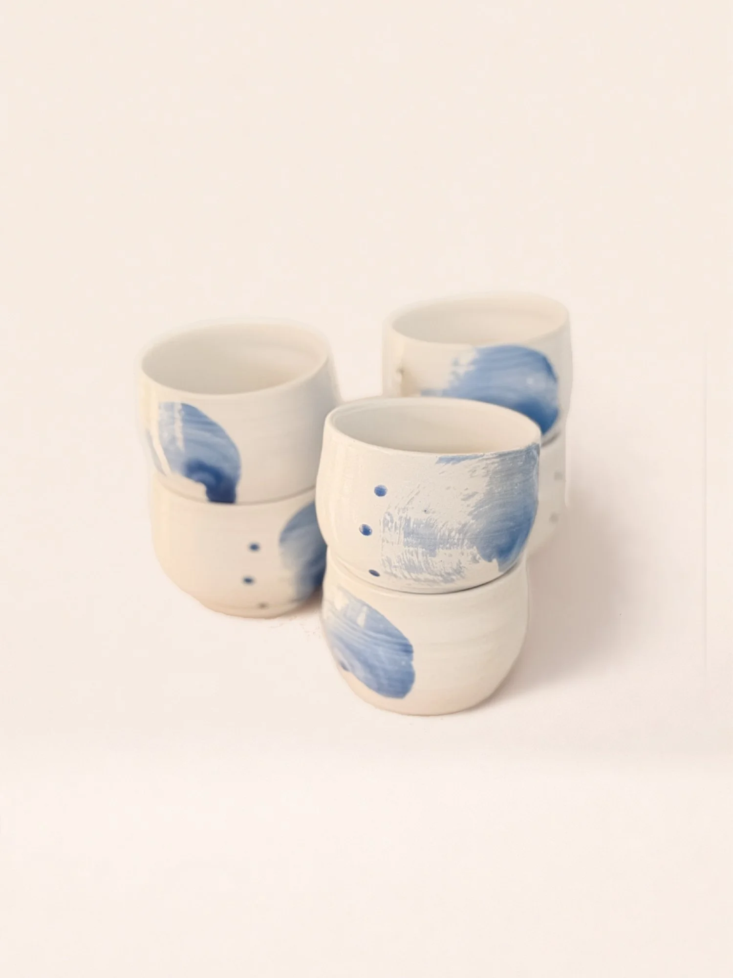 Six white ceramic cups with blue abstract brushstroke designs stacked together on a white background.