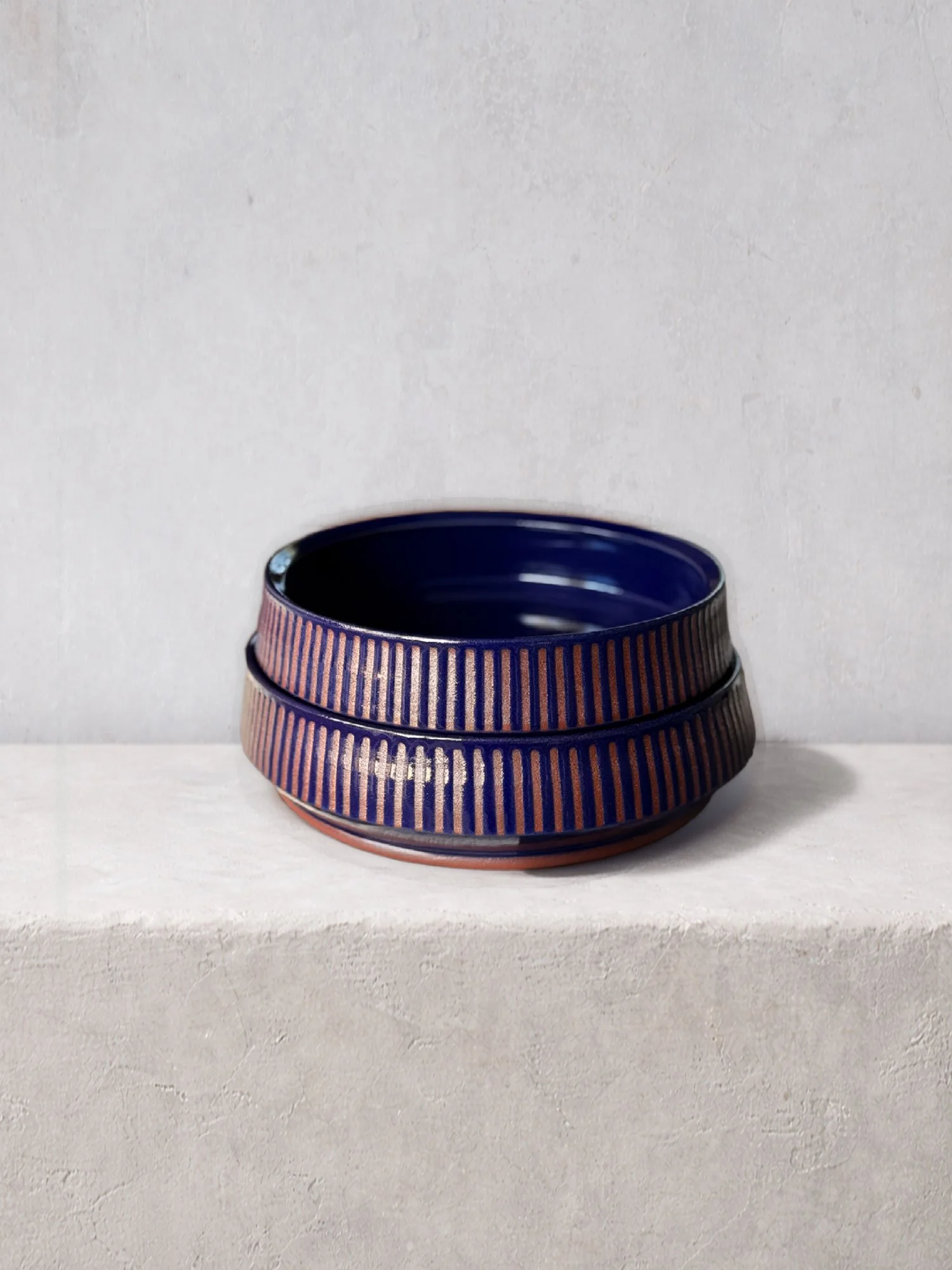 Handmade ceramic bowl with deep blue glaze and vertical ribbed texture, photographed on a minimalist background.