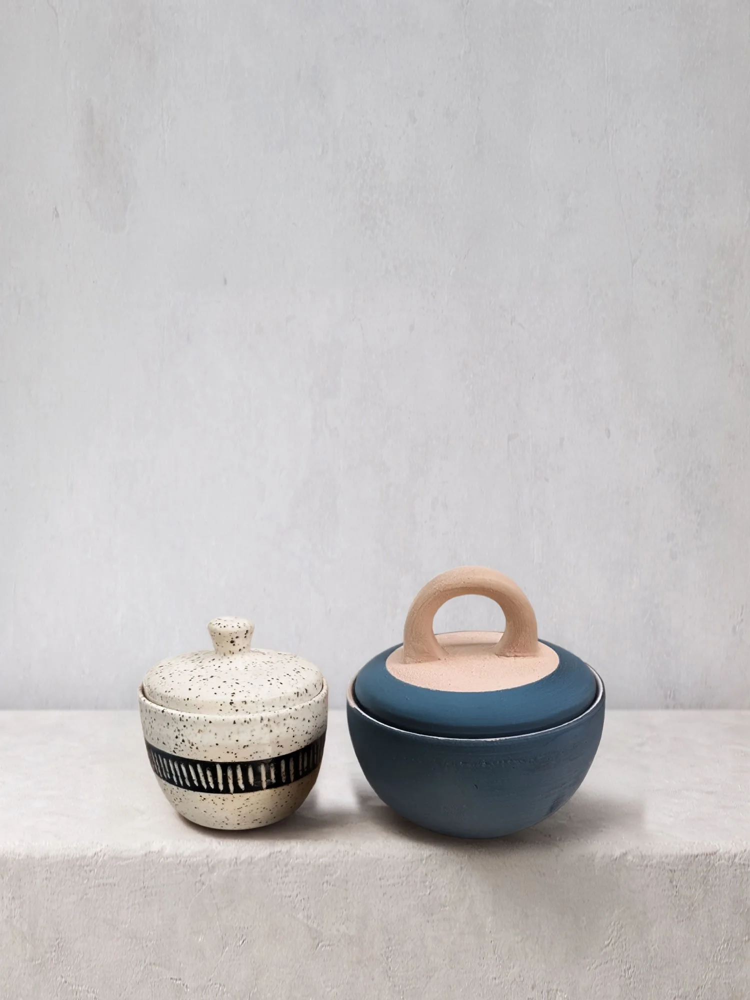 Handmade ceramic cups and a tumbler in natural clay tones with carved and banded details, styled in a minimalist setting.