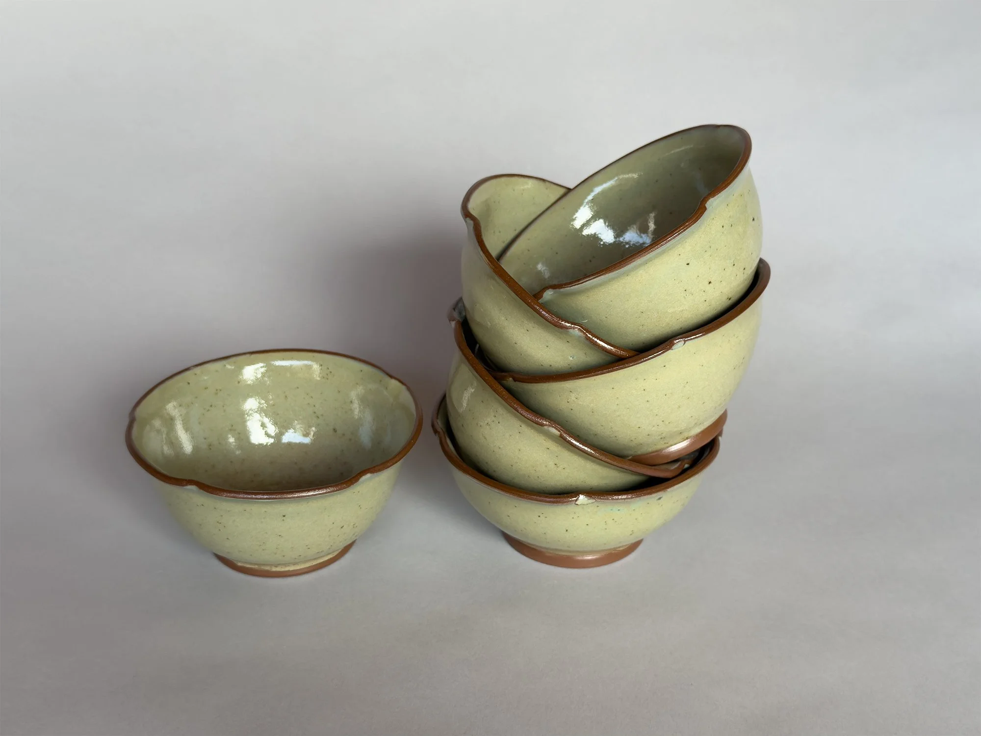 Stacked handmade ceramic nesting bowls with speckled sage green glaze and organic hand-formed edges by Jeanette Burgett Ceramics on a soft neutral background.