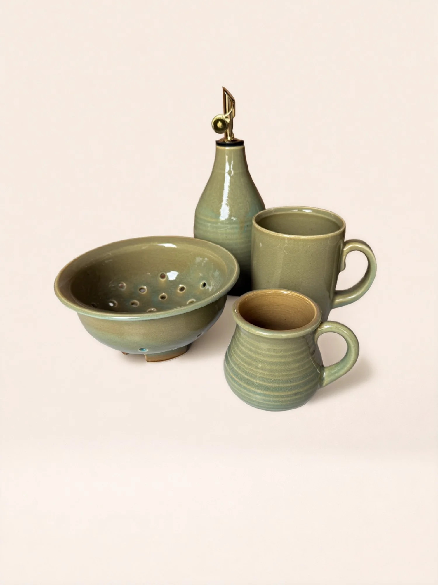 Set of five green ceramic kitchenware items including two mugs, a pitcher, a bowl with holes, and a squeeze bottle with a gold-colored lid and spout.
