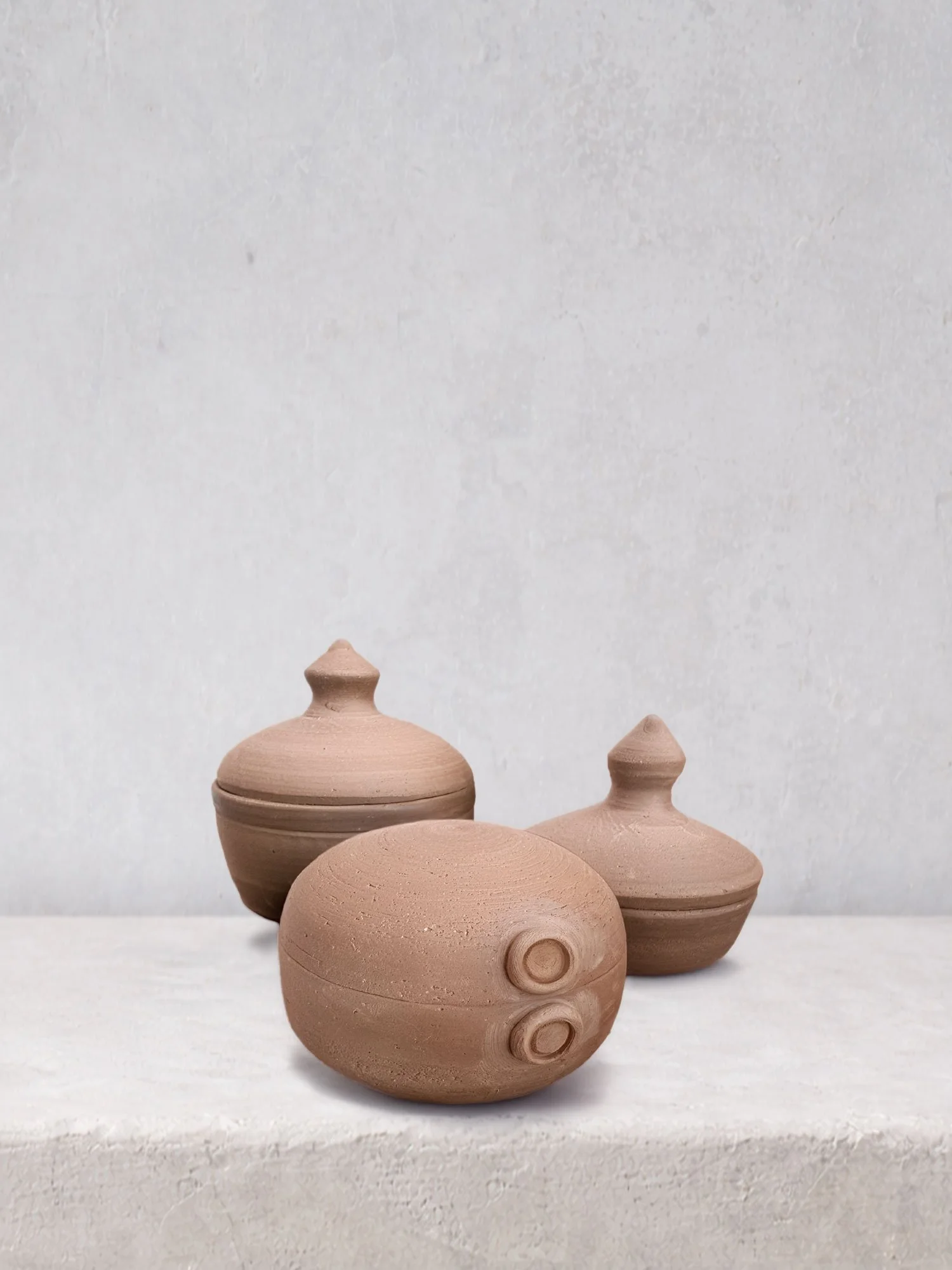 Three handmade lidded ceramic containers in natural clay, featuring simple forms and warm, earthy tones.