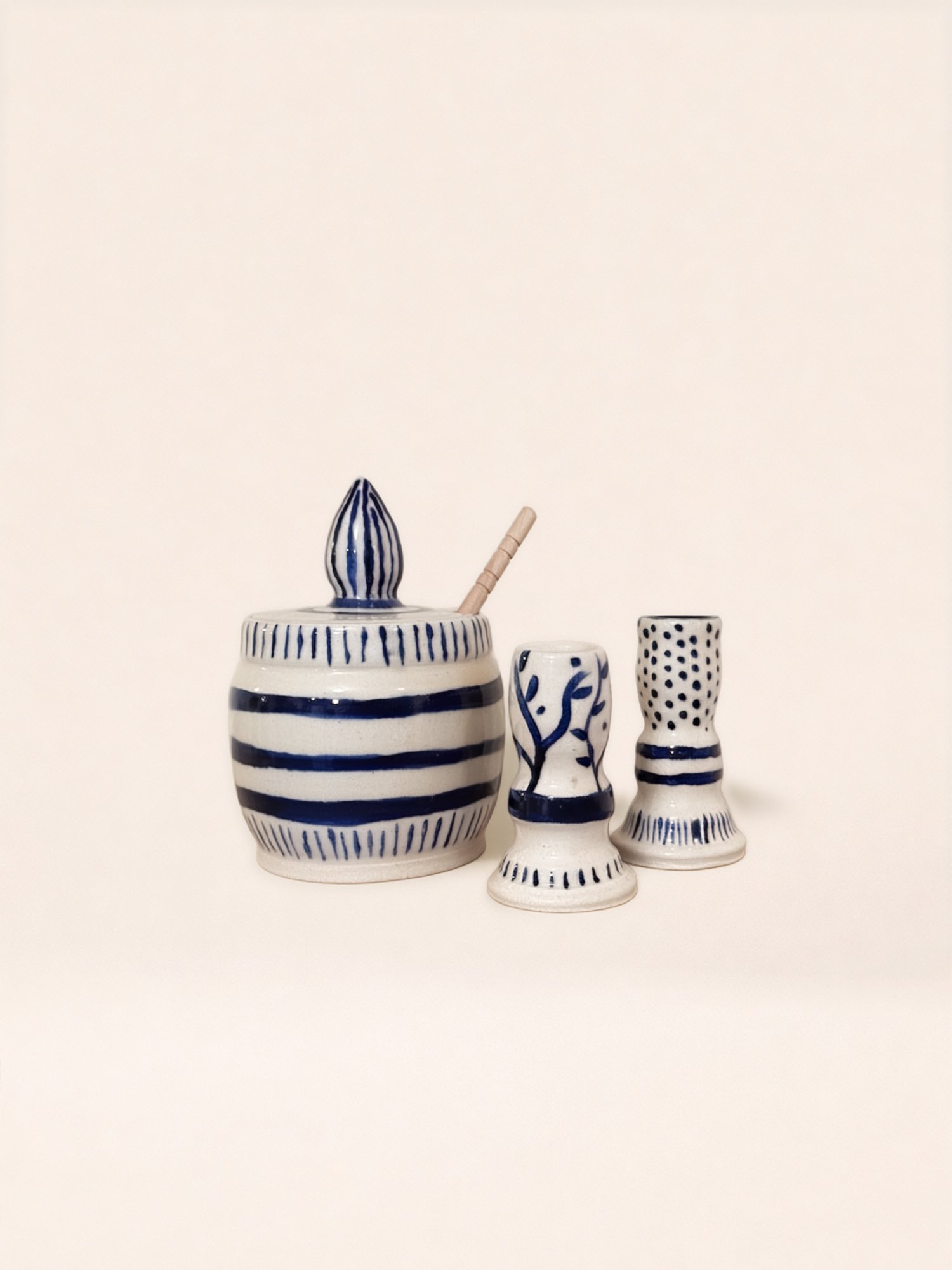 Three ceramic containers with blue and white patterns, one large with a lid and a stick, and two smaller with different dotted and striped designs.