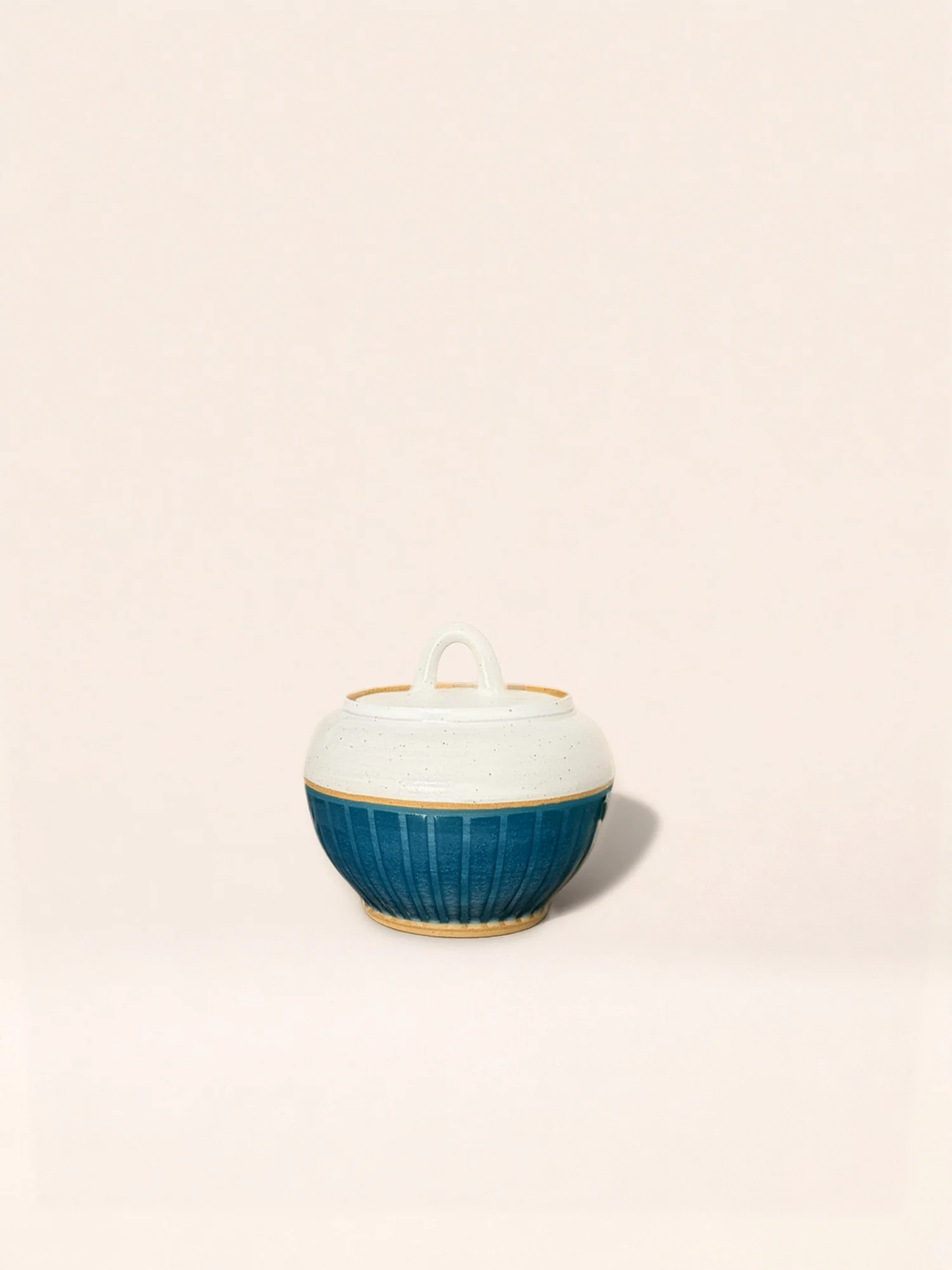A ceramic bowl with a white top half and a blue bottom half, featuring vertical ridges, placed on a plain white background.