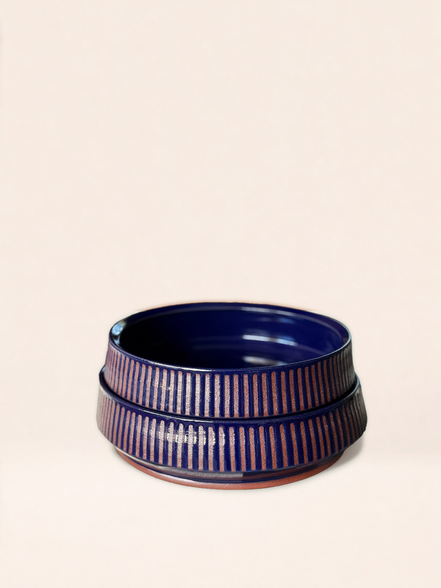 A ceramic bowl with a dark blue interior and a brown and blue striped exterior, placed on a plain light-colored surface.