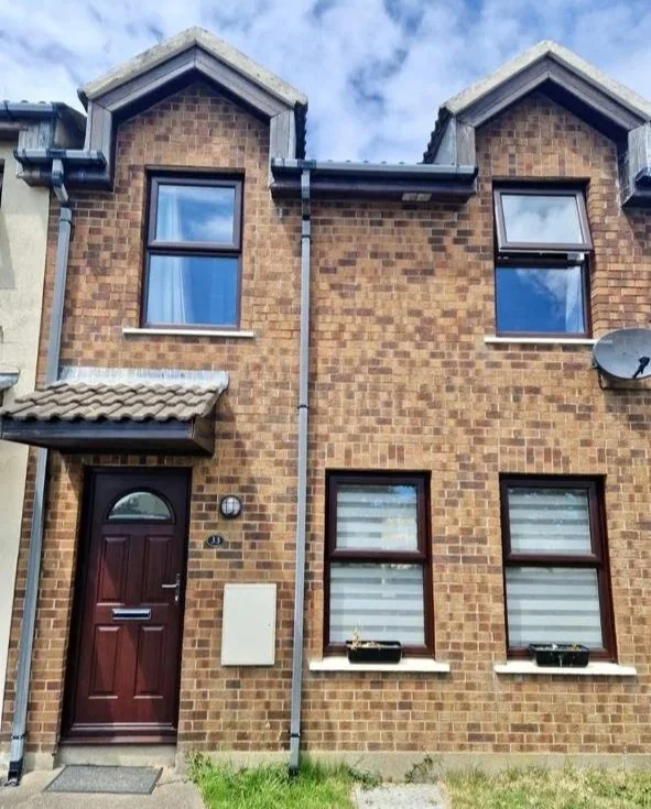 Brick townhouse with two stories, four windows, a dark red front door, satellite dish, and a white utility box on the exterior wall.