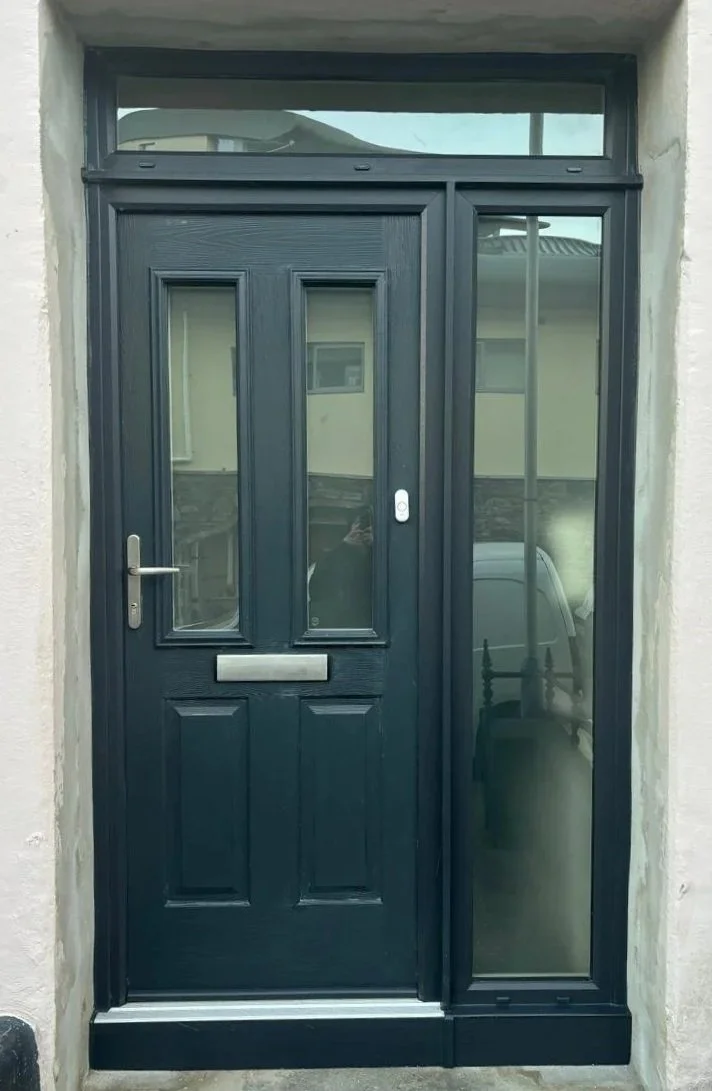 Black front door with glass panels and a letterbox, flanked by a large glass side panel, set in a white exterior wall.