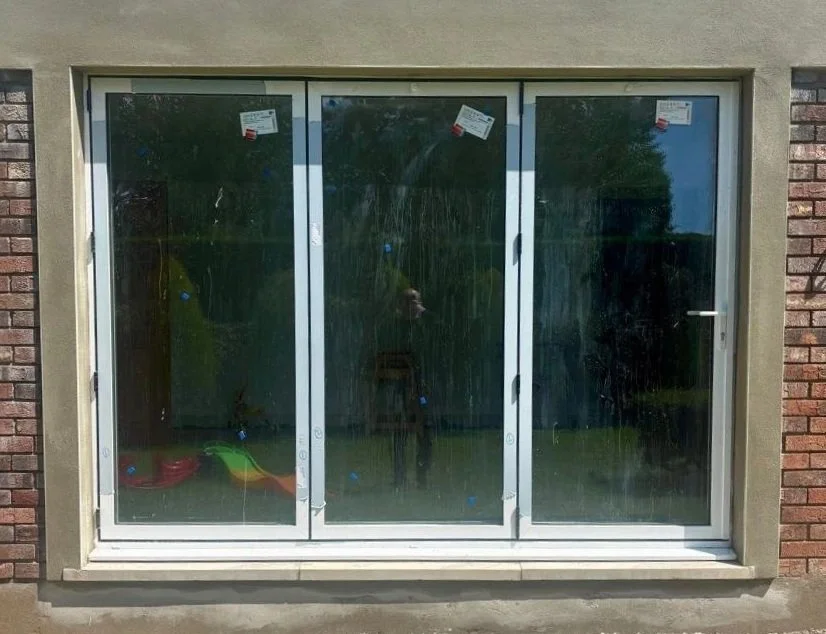 Dirty glass sliding door with three panels, attached to a brick and cement wall, with children's toy in the lower left corner.