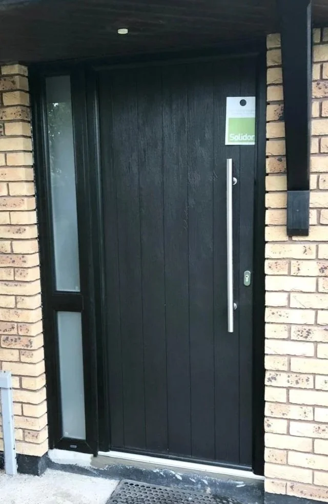 Black front door with a long vertical handle, a small window to the side, and a green sign reading 'Solidar' on the door.