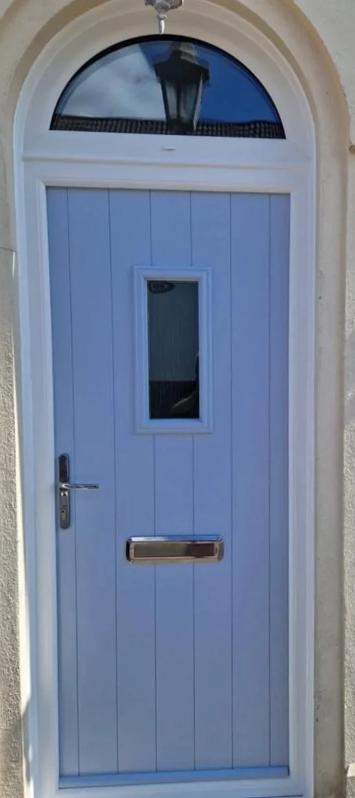 Light blue front door with a small window, a mailbox slot, and a silver handle, topped by an arched window with a lantern reflection.