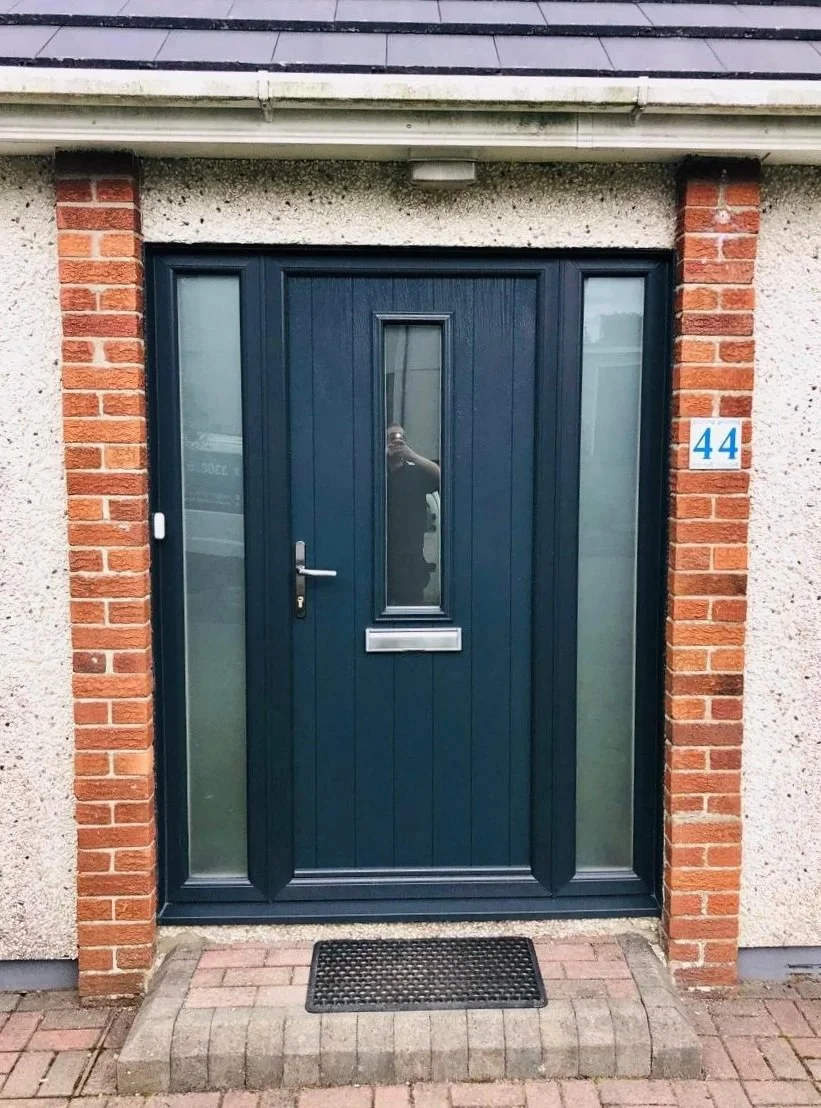 Blue front door with narrow window in the center, flanked by two vertical windows, surrounded by brick and stucco walls, with house number 44 on a blue and white plaque to the right.