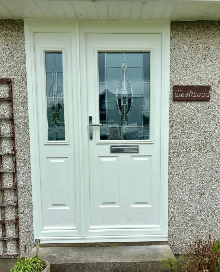 White front door with decorative glass panels, a mailbox slot, and a door handle, next to a textured wall and a wooden sign that reads 'Westwood'