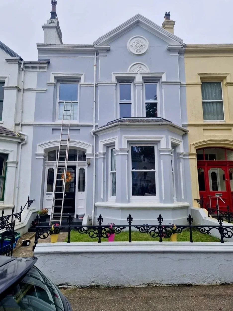 Front view of a Victorian-style row house painted white, with a small front yard, black iron fence, and a ladder leaning against the house.
