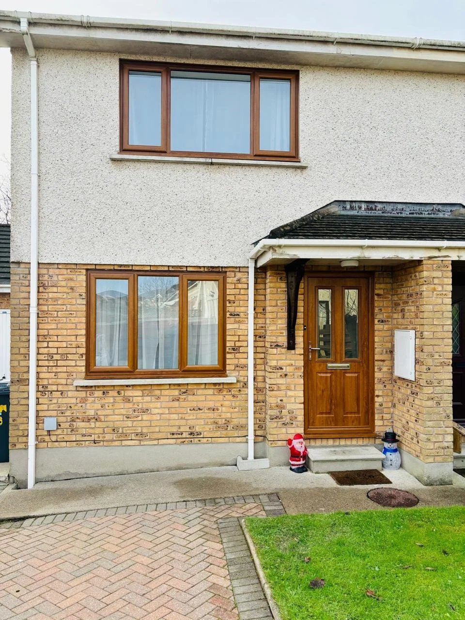 Front entrance of a brick and stucco house with holiday decorations, including a Santa figure and a snowman, on the steps leading to the wooden front door.