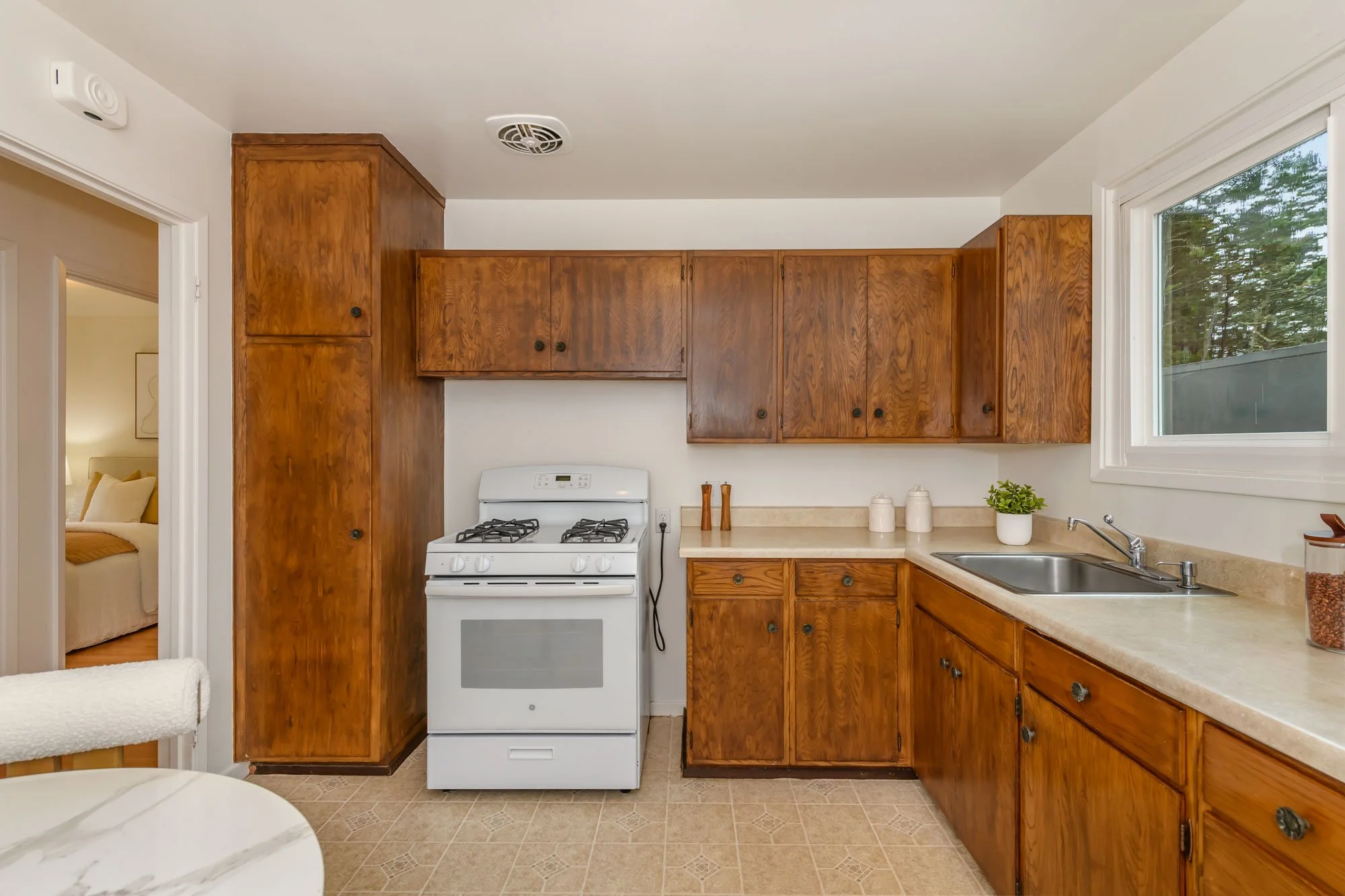 Kitchen with wooden cabinets, white stove, beige countertop, and a window.