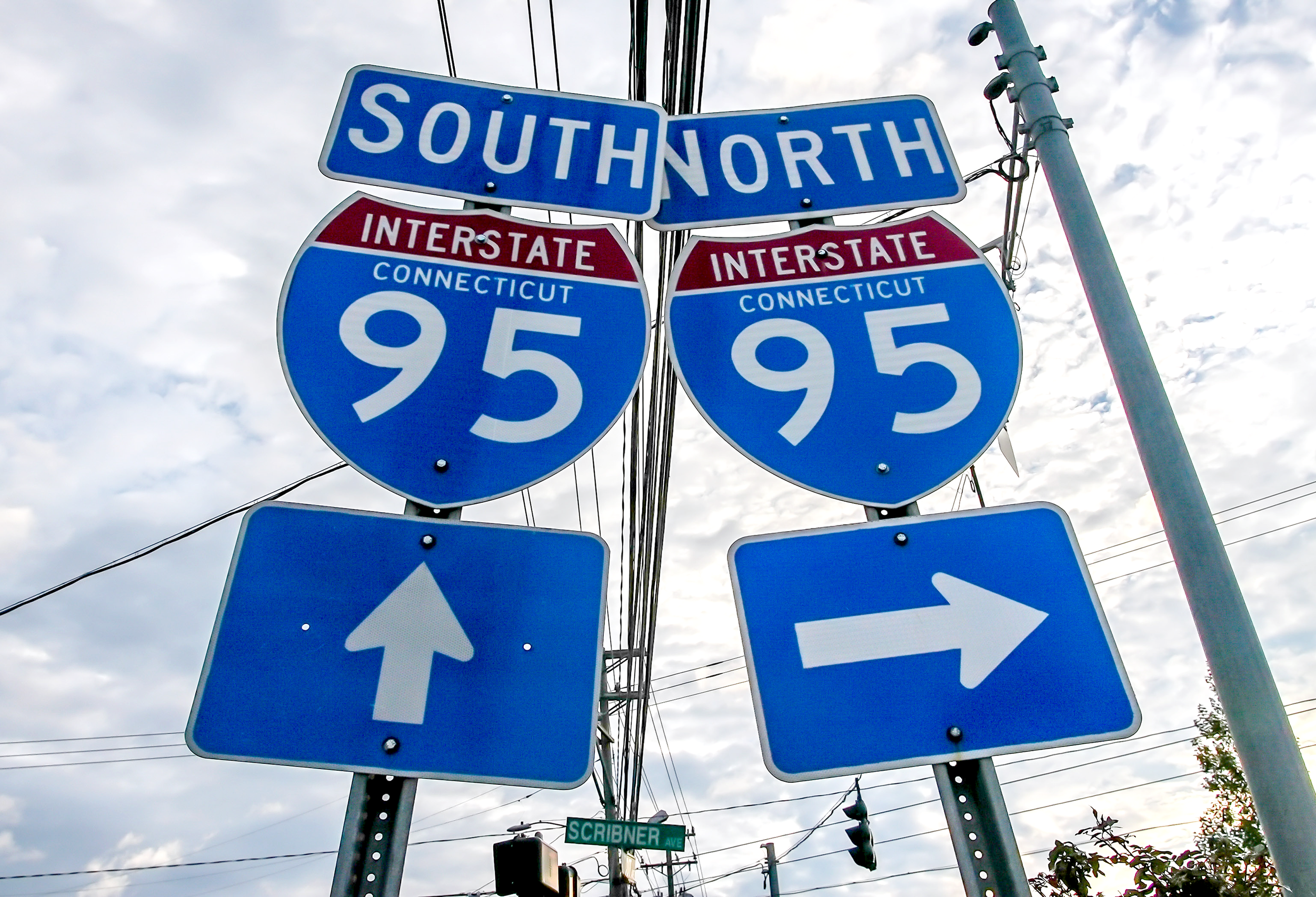 Directional road signs for South North, Connecticut Interstate 95, with arrows pointing straight ahead and to the right, positioned under a cloudy sky.