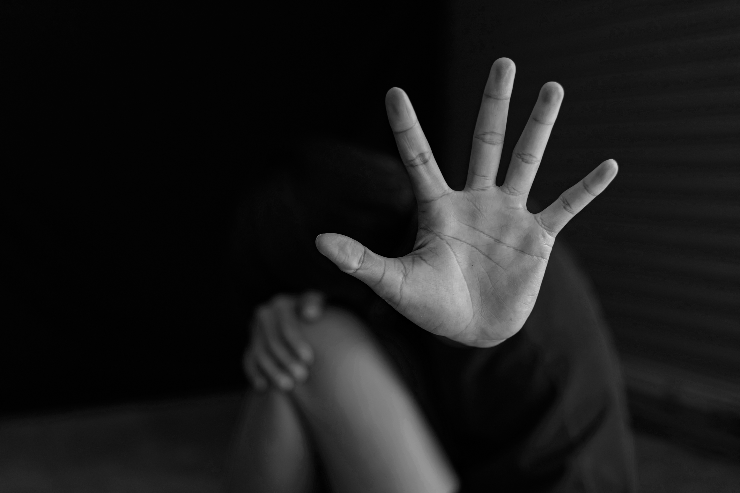 Black and white photograph of a hand with fingers spread, reaching towards the camera, with a person's torso and a hand resting on their knee visible in the background.