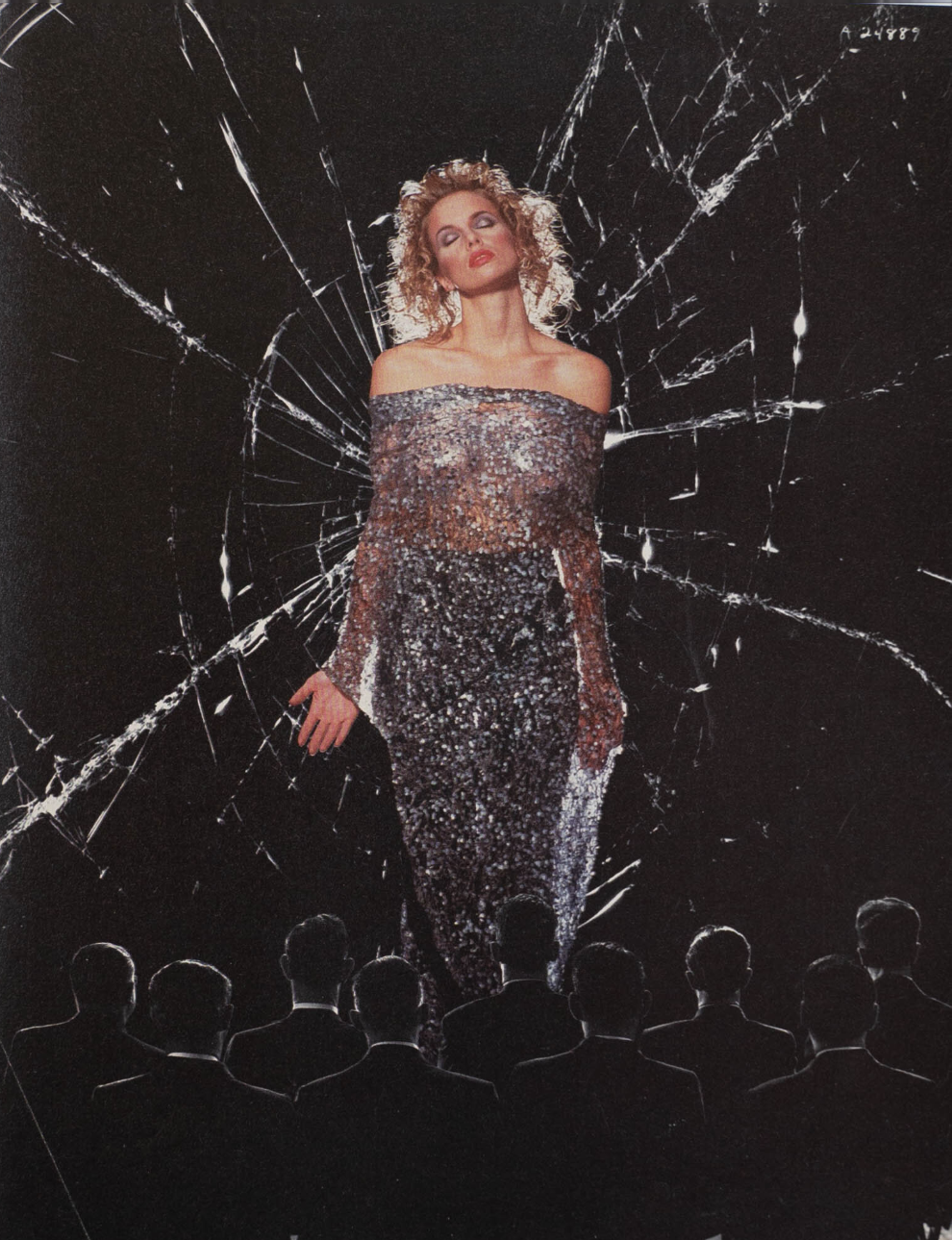A woman with curly blond hair and dramatic makeup stands in front of a cracked black background, wearing a sparkly off-shoulder dress, with seven men in suits seen from behind at the bottom.