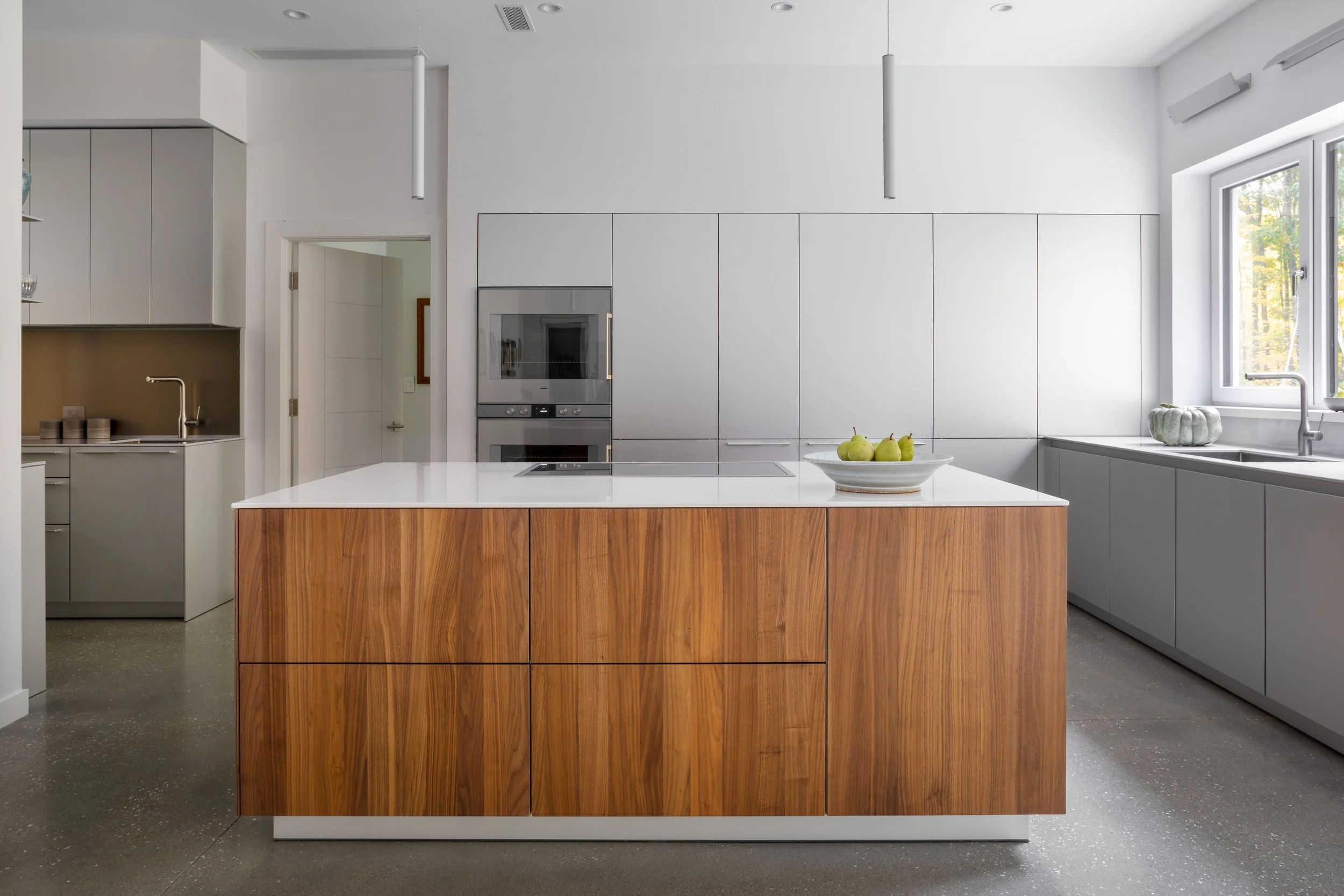 Modern kitchen with white cabinets, a wooden island with a white countertop, and a window showing outdoor trees.