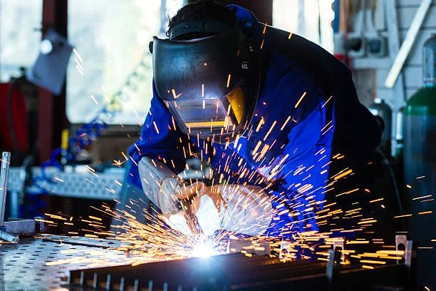 A person welding metal in a workshop, sparks flying.