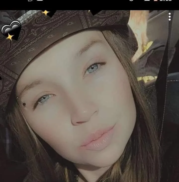 A woman with light skin, light blue eyes, and long brown hair wearing a wide-brimmed patterned hat.