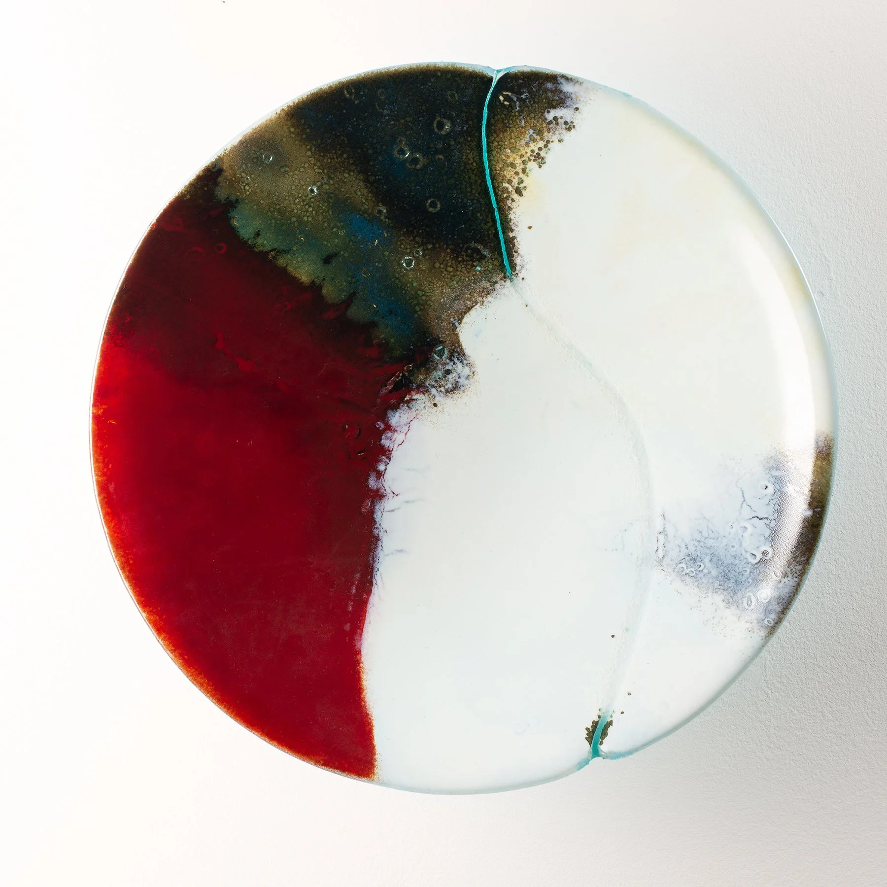 An abstract glass wall hung bowl with splashes of red, black, green, and white colors, featuring a visible crack on the rim.