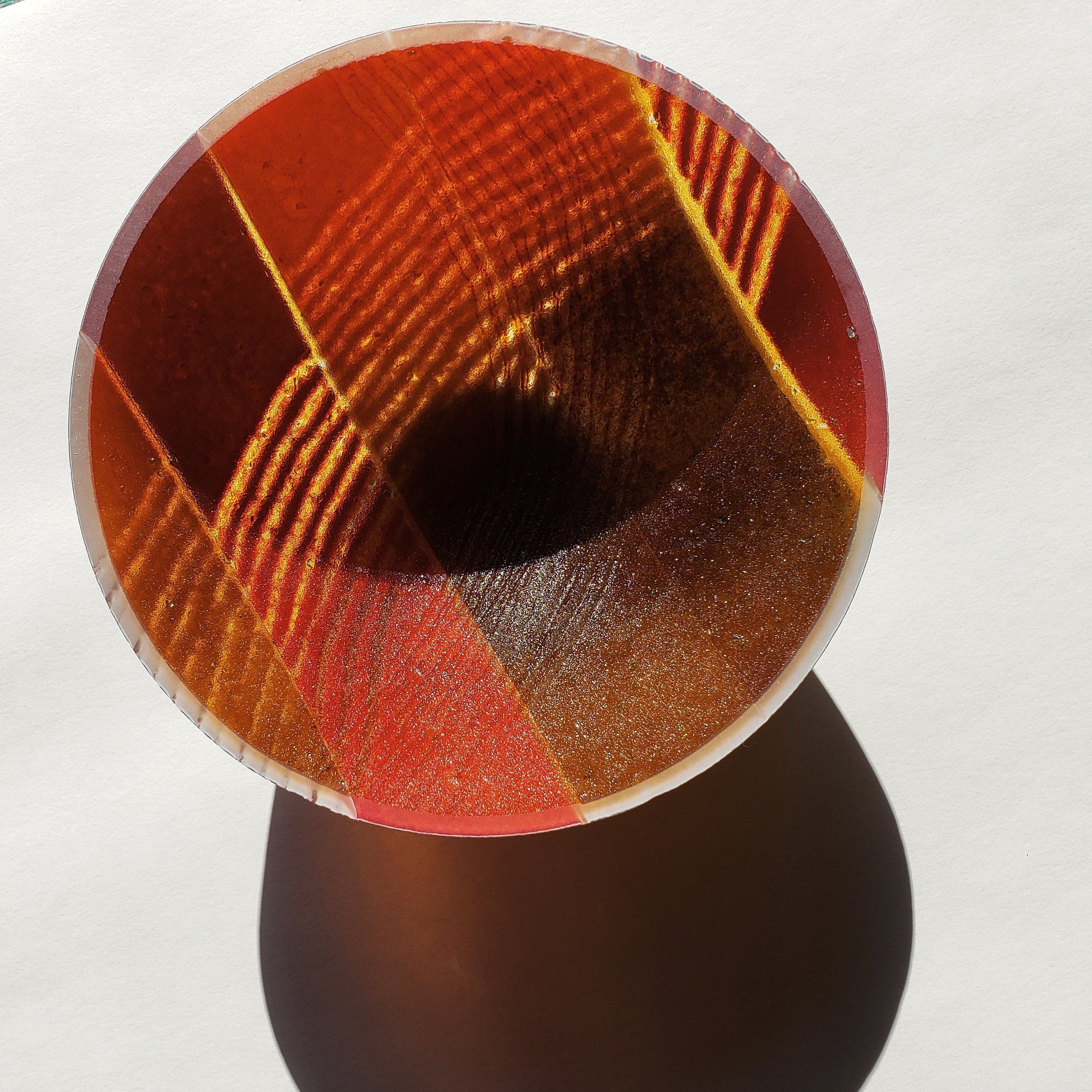 The top view of a circular color palette with various shades of red, orange, brown, and gold, with a shadow cast on the white surface beneath.