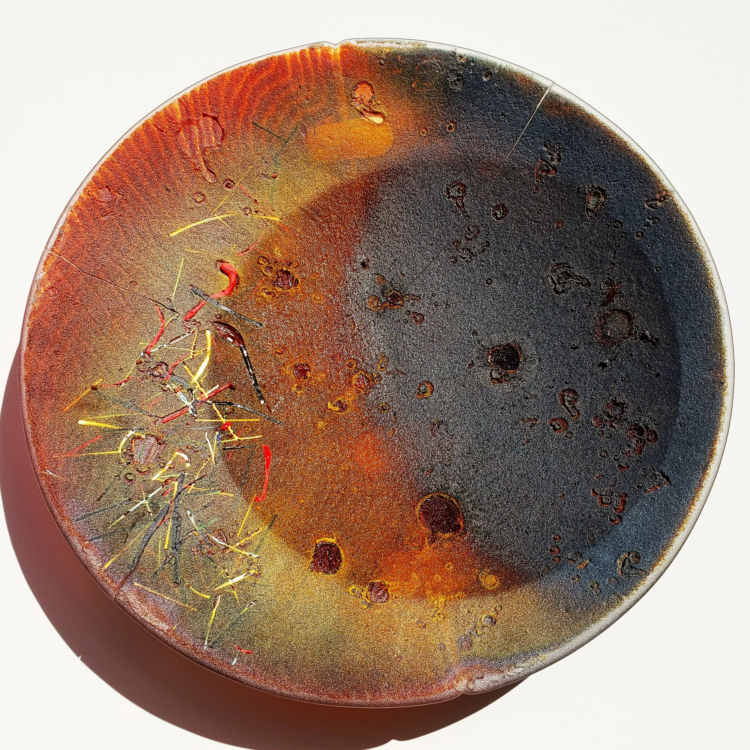 An abstract wall hung glass bowl with surface colonies in various colors, including black, yellow, and red, on a white background.