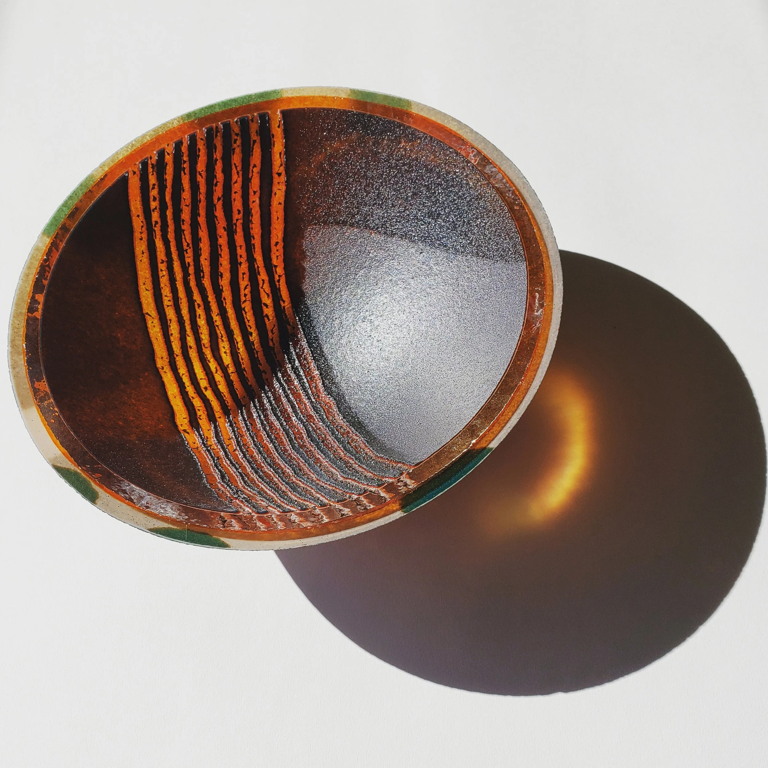 Cross-section of a metal pipe with rust and corrosion inside, casting a shadow on a white surface.