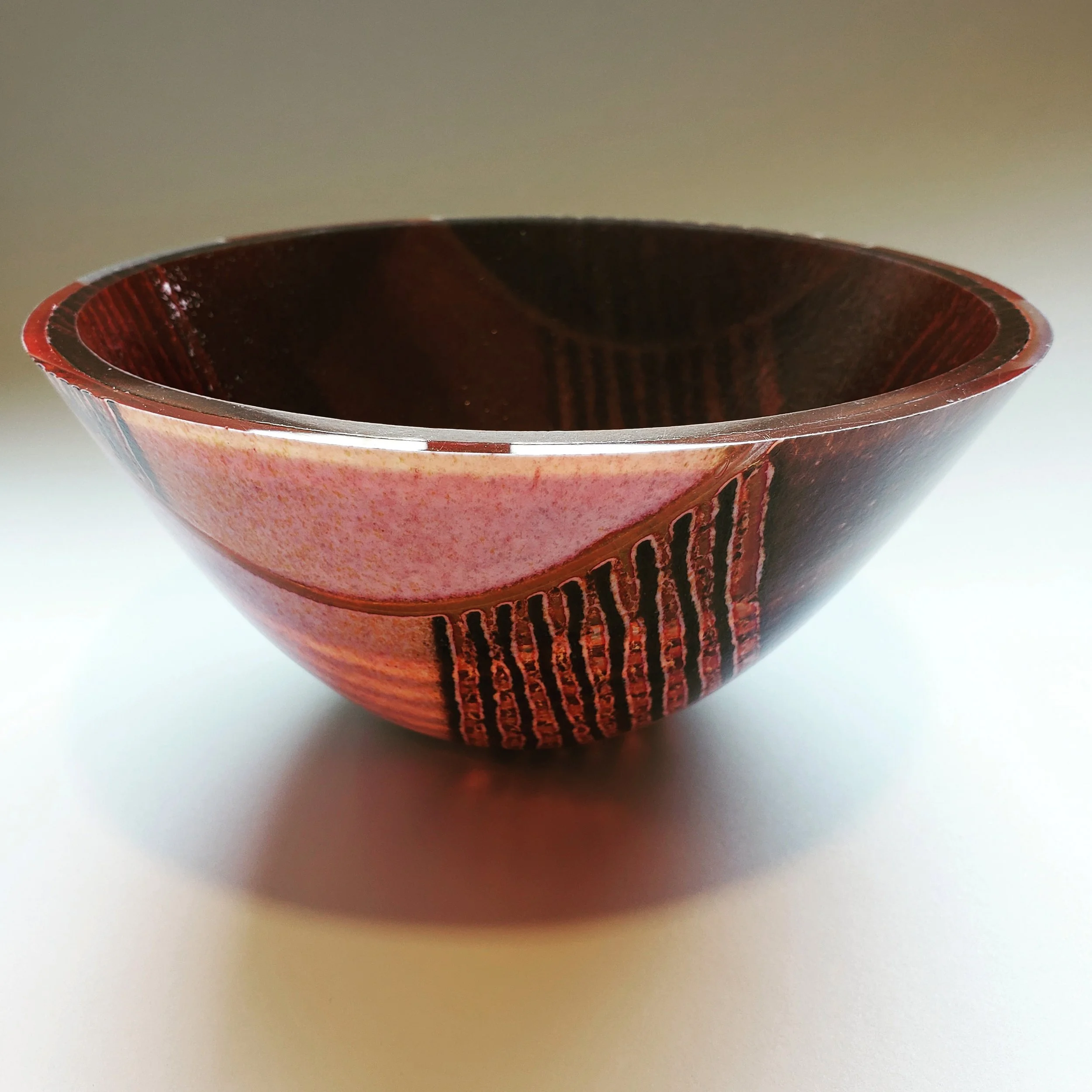 A decorative ceramic bowl with abstract red and black patterns, placed on a white surface.