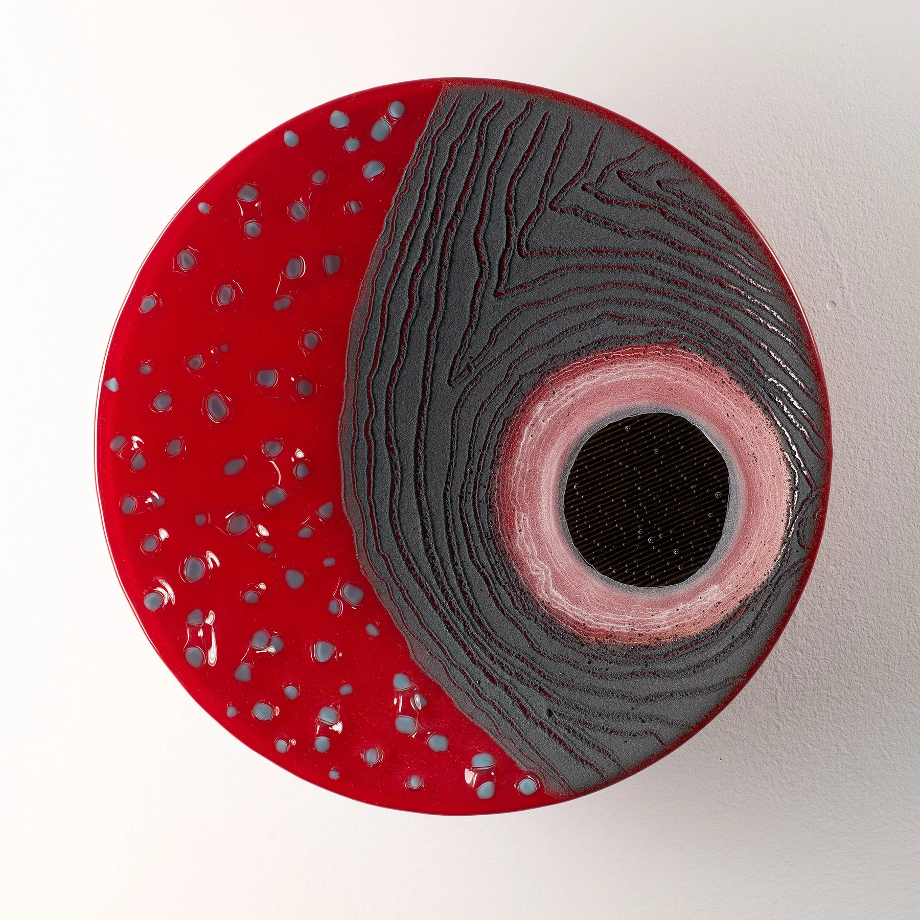 Abstract circular artwork with red, black, and pink concentric patterns, textured black lines, and blue dots on a white background.