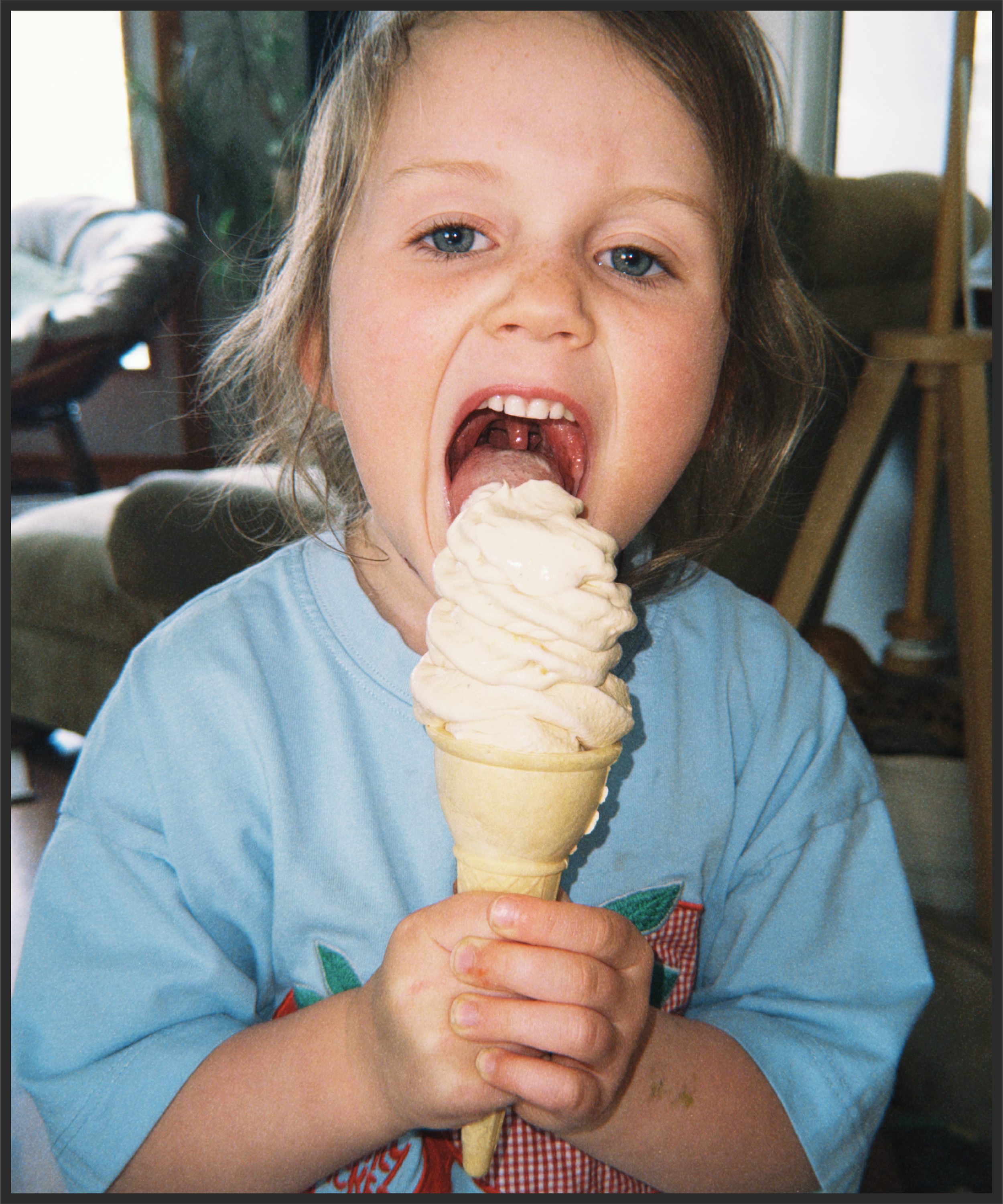A young child with light brown hair and blue eyes is eating a large scoop of vanilla ice cream in a cone.