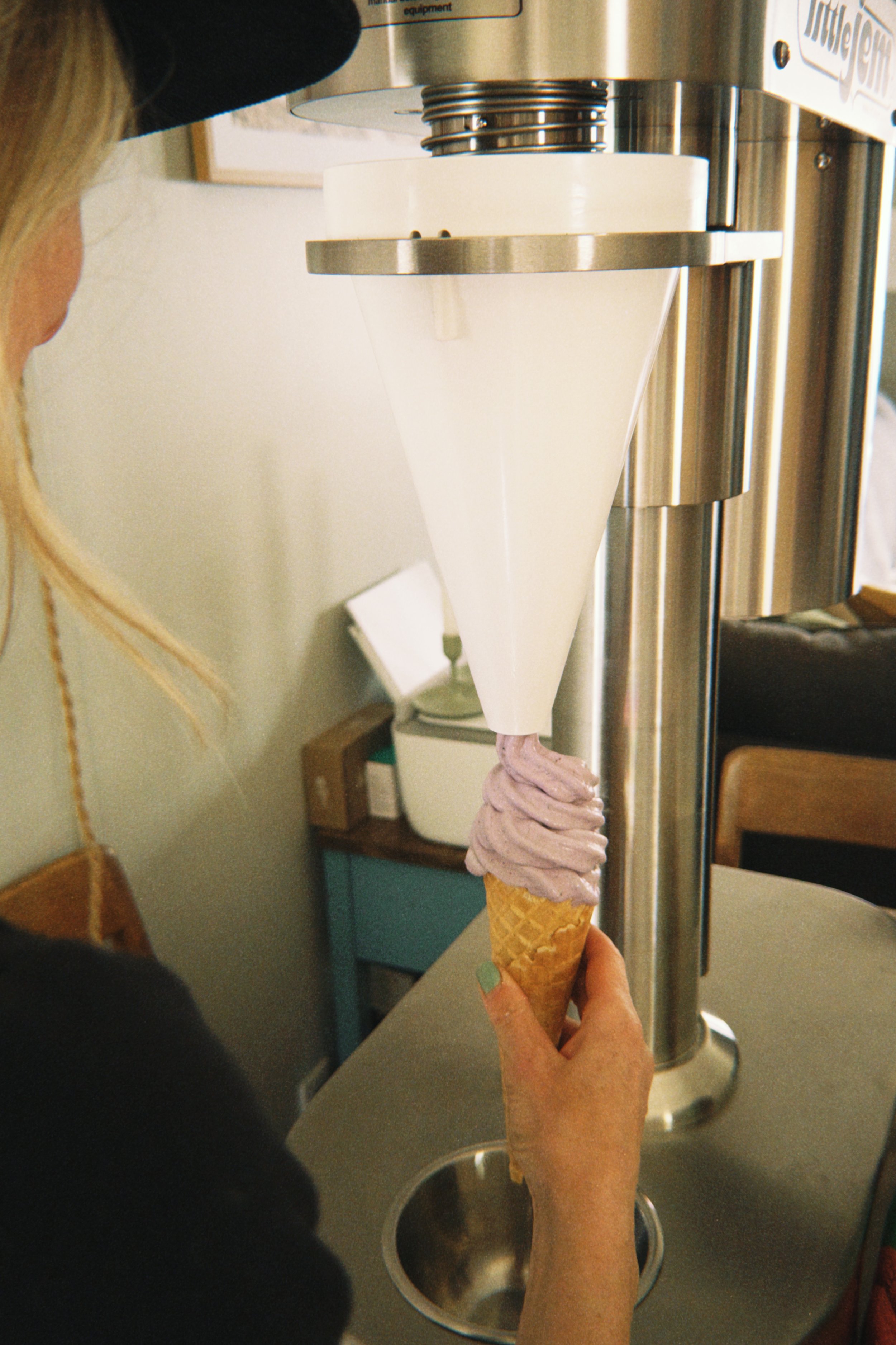A person holding an ice cream cone under a soft serve ice cream machine.